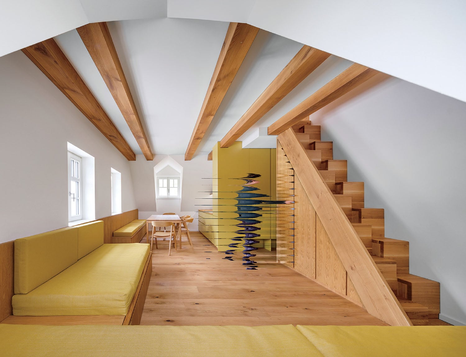 A room with a yellow couch and wooden stairs.