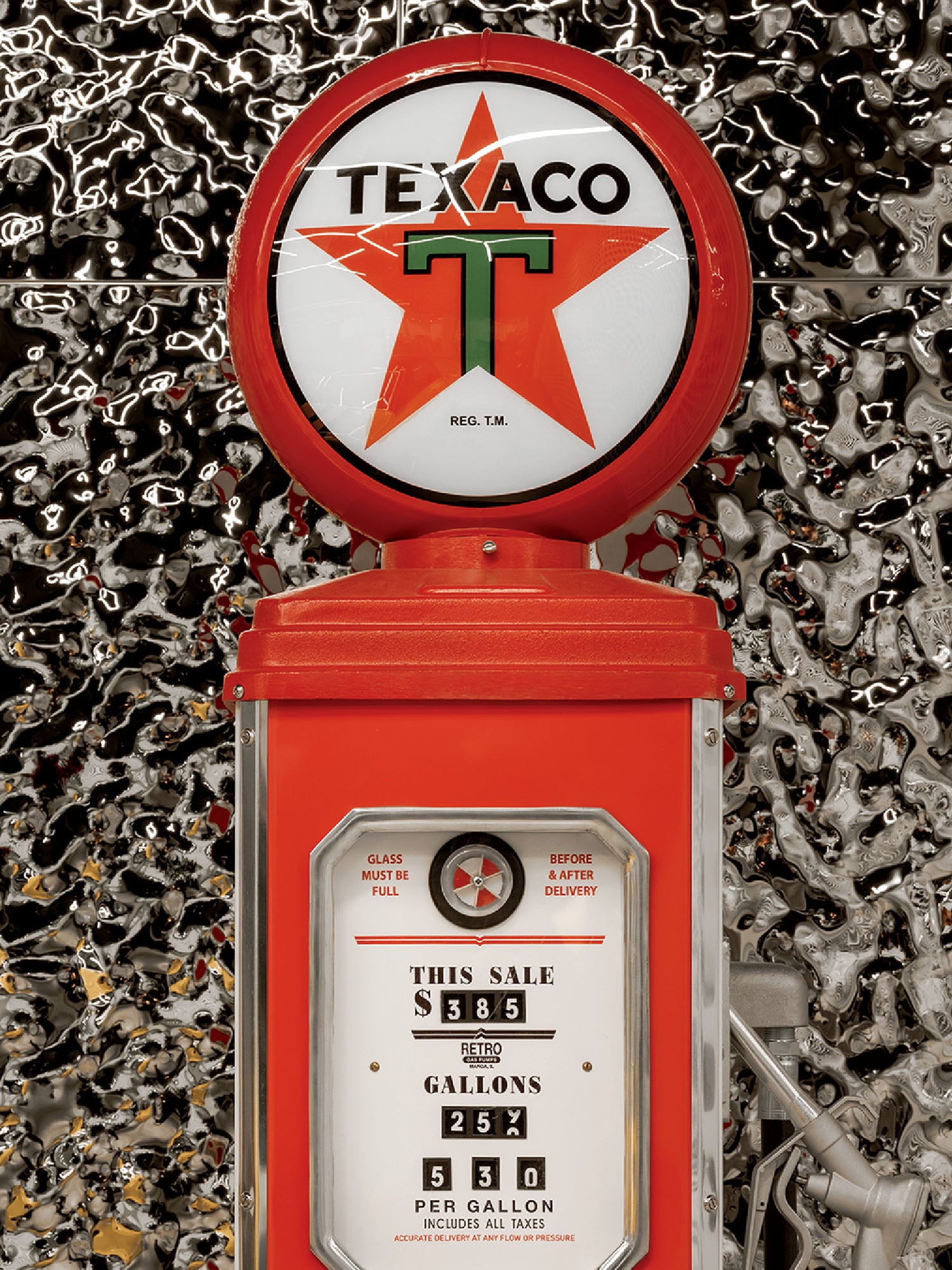 A vintage red Texaco gas pump with a round Texaco logo on top, shows prices and gallons display, set against a metallic, reflective background.