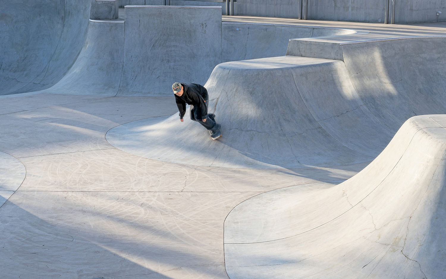 A person skateboards on the curved surfaces of a concrete skate park under daylight.