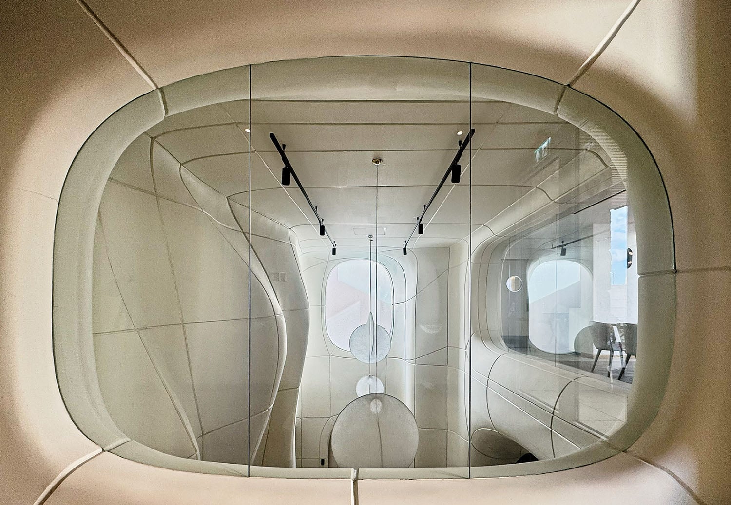 A modern, futuristic white room with rounded walls and large glass panels, featuring minimalistic lighting and geometric shapes.