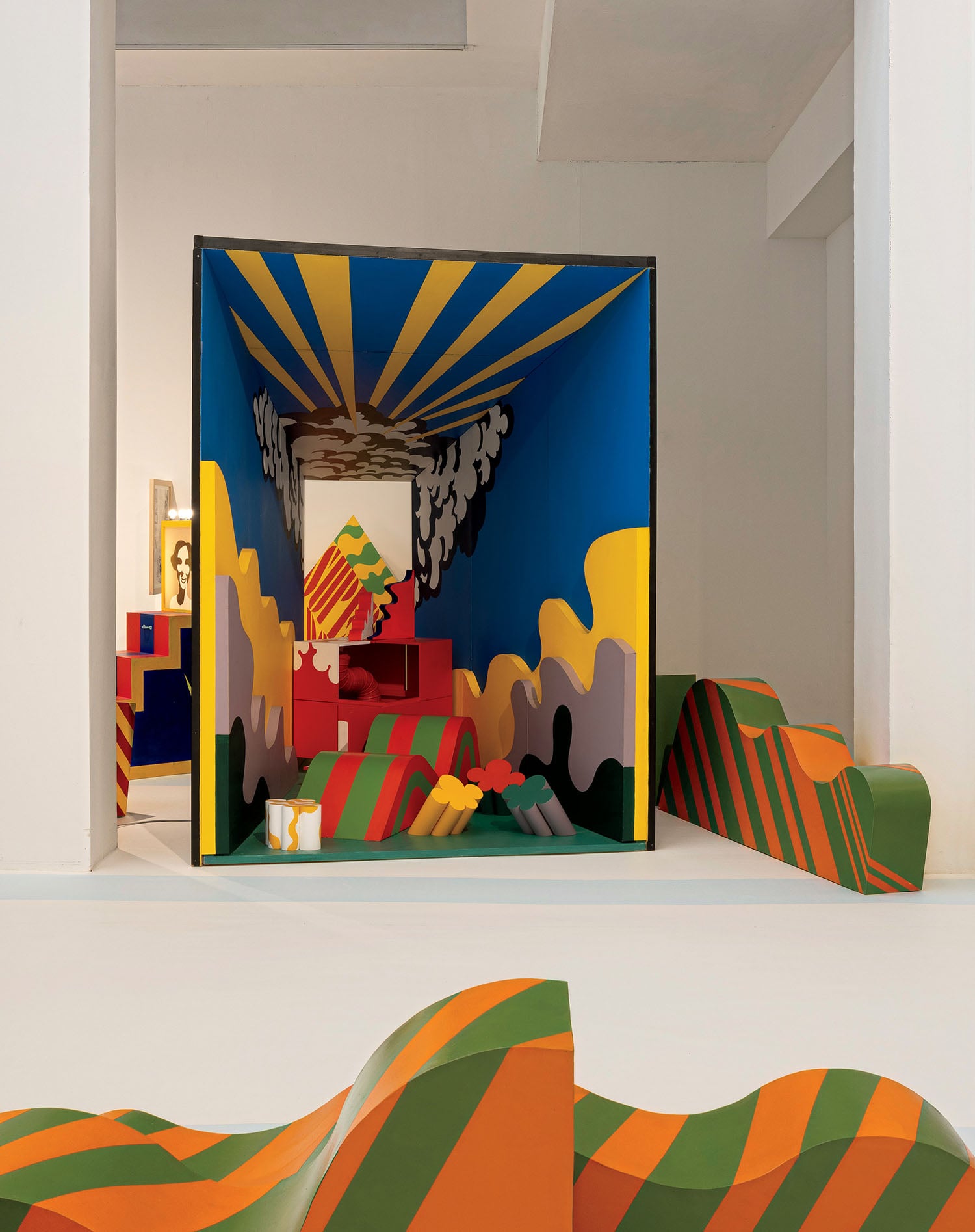 A colorful, abstract installation with geometric and wavy shapes in a gallery space, featuring bold yellow, blue, green, orange, and red patterns.