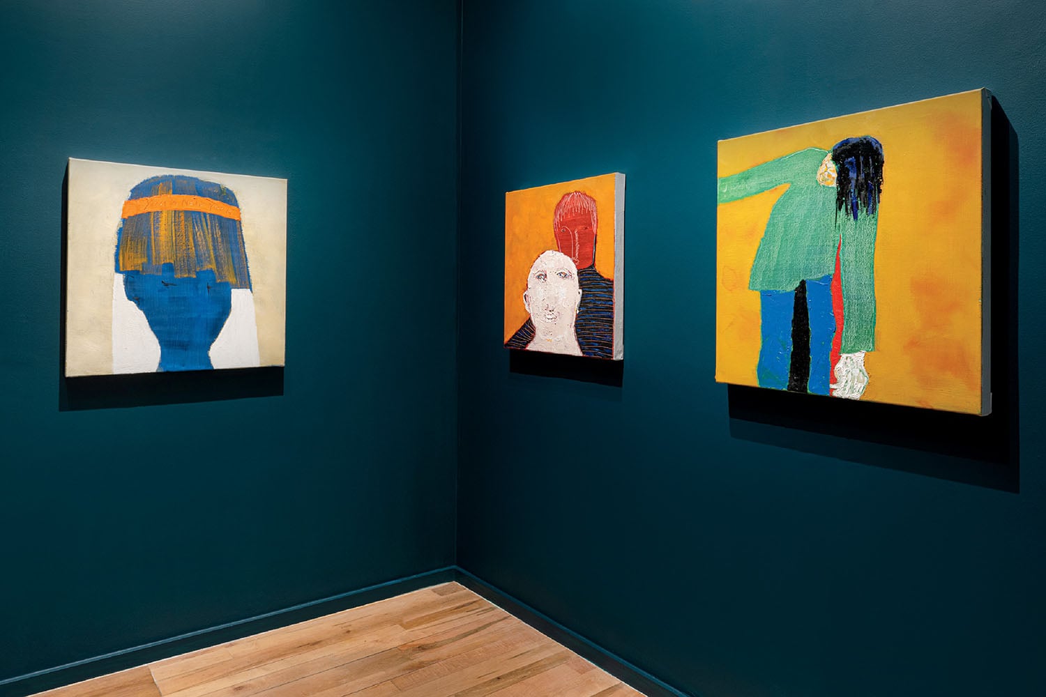 Three colorful abstract paintings, each depicting stylized human figures, are displayed on dark teal walls above a light wooden floor in an art gallery.