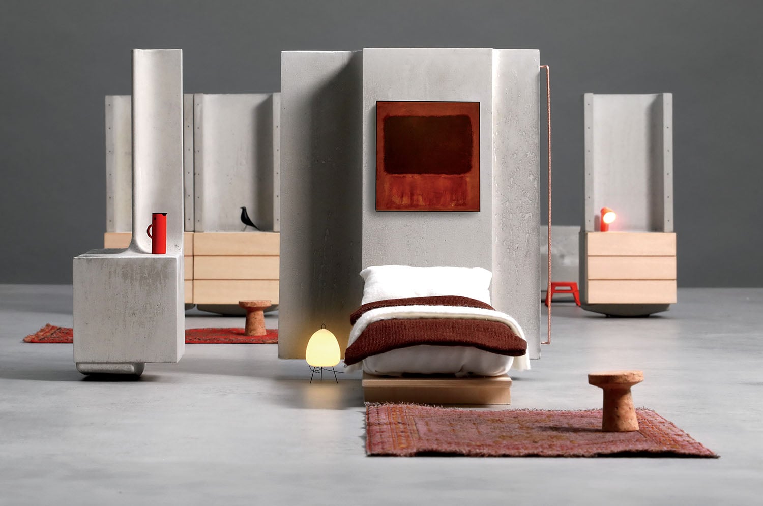Modern minimalist bedroom with a single bed, small lamp, side tables, abstract wall art, and red rugs, featuring concrete and wood elements against a gray background.