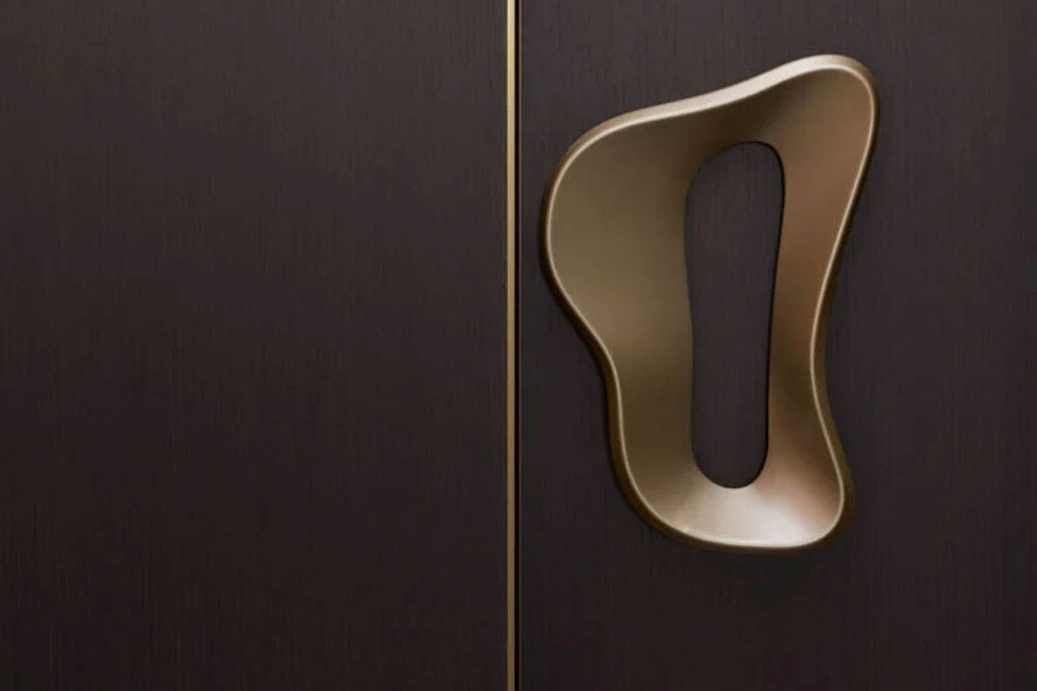 A close-up of a dark wooden door with a large, abstract-shaped metallic handle on the right side.