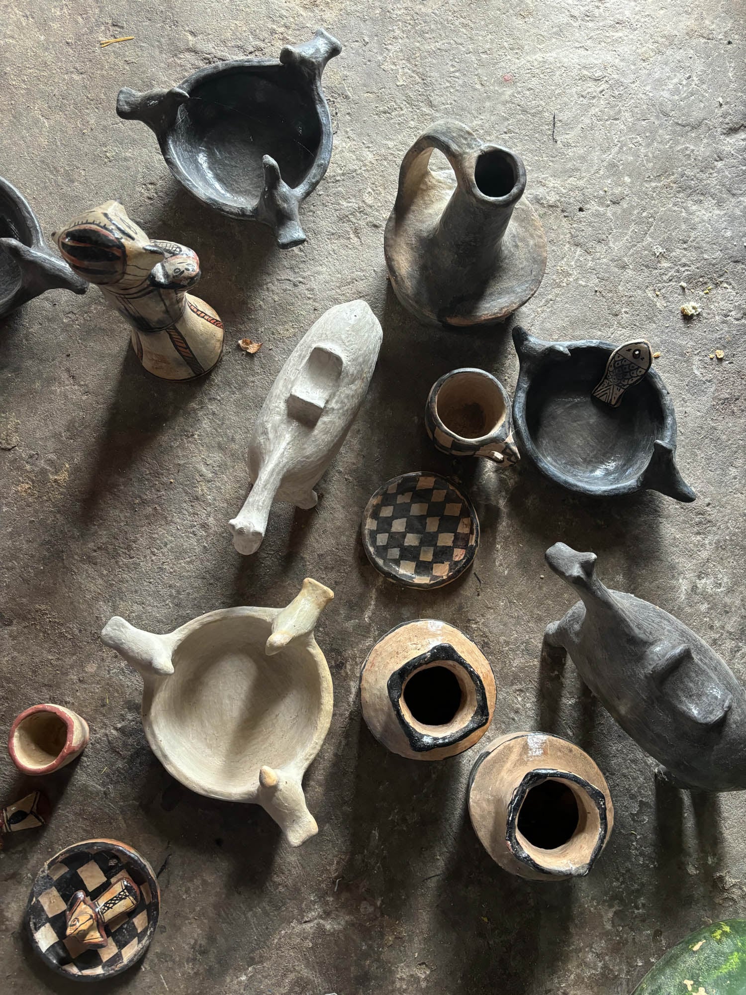 Various handmade clay pottery pieces, including bowls, jugs, and animal-shaped vessels, are arranged on a textured stone surface.