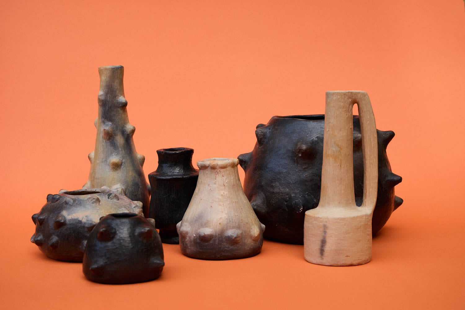 A group of ceramic vessels with bulbous, spiked surfaces in varying shades of brown and black, arranged against an orange background.