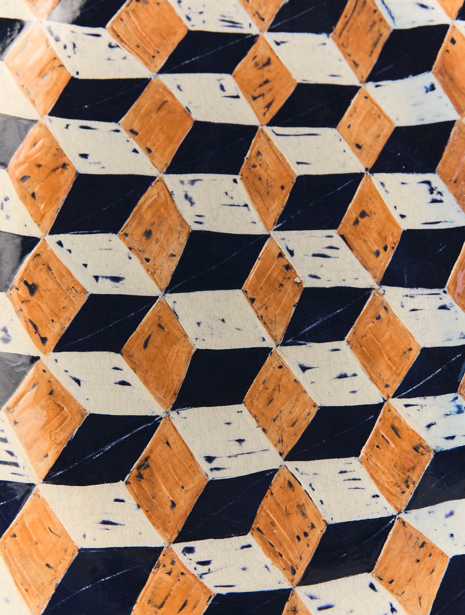 Close-up of a geometric tile pattern featuring alternating orange, black, and white diamond shapes arranged in a three-dimensional cube effect.