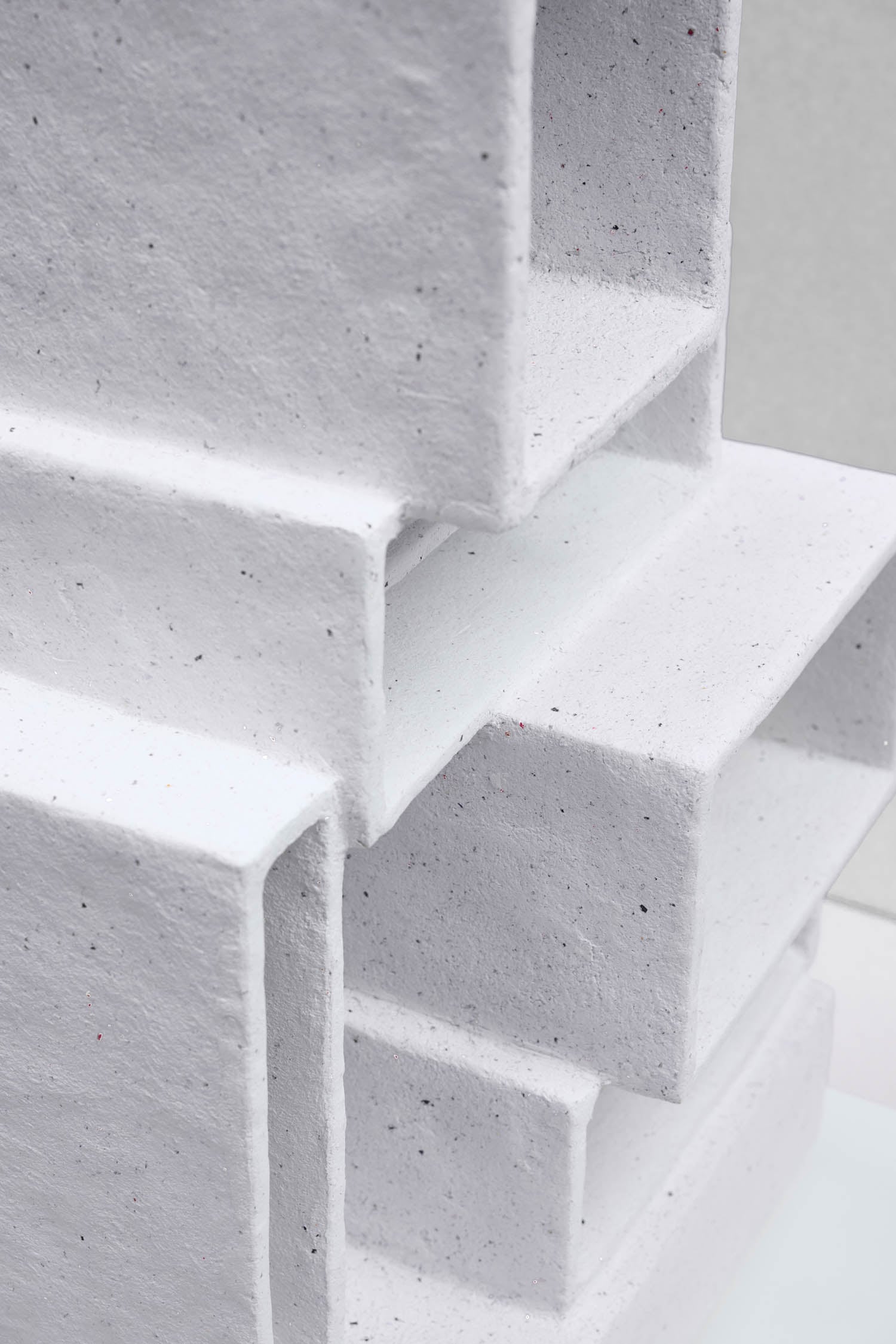Close-up of stacked, white, rectangular structures made from a textured, paper-like material, arranged in a geometric pattern.