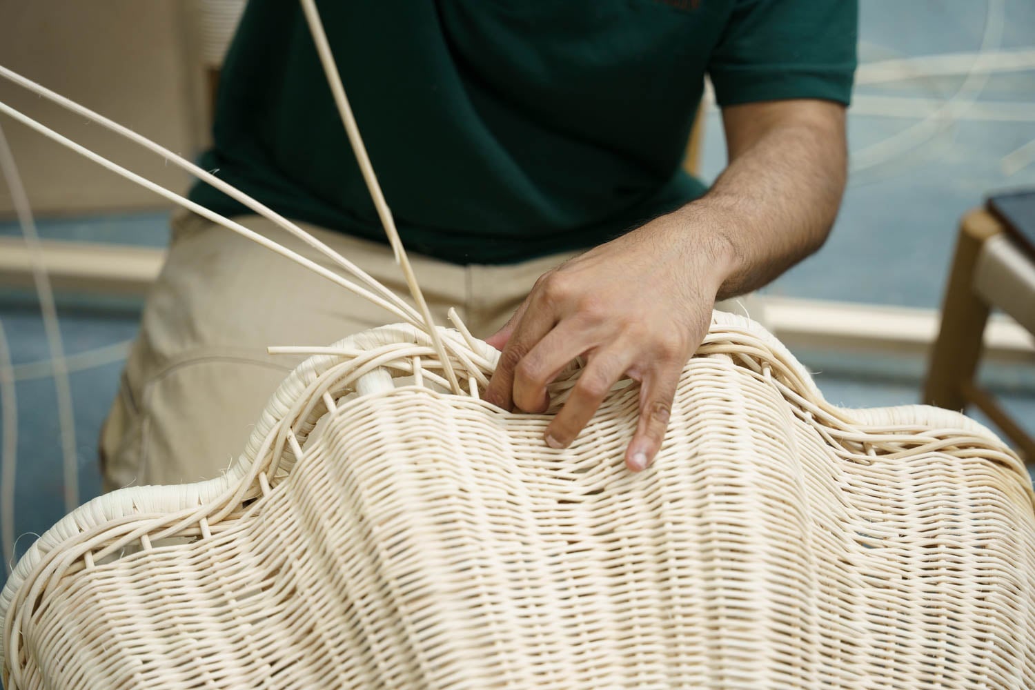 A person weaving thin strips of material to make or repair a wicker chair, with only their hands visible.