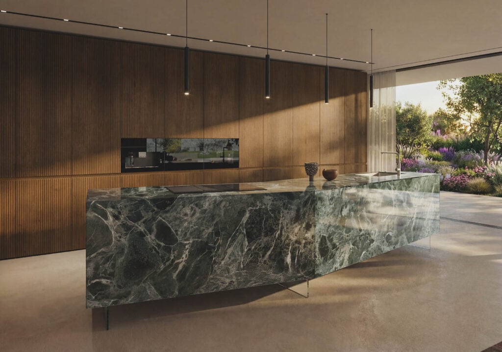 Modern kitchen with a large marble island, wooden paneled wall, hanging pendant lights, and floor-to-ceiling windows overlooking a garden.