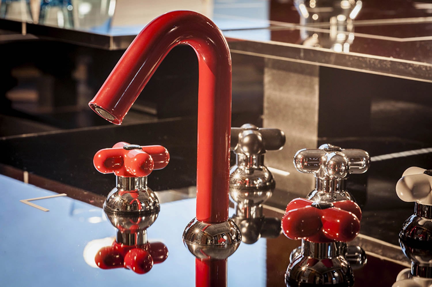 Red, curved faucet with matching and chrome cross-shaped handles, set on a glossy black countertop.