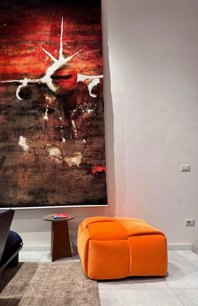A modern room with a large wall art of an airplane, a small side table with magazines, and an orange ottoman on a gray rug.