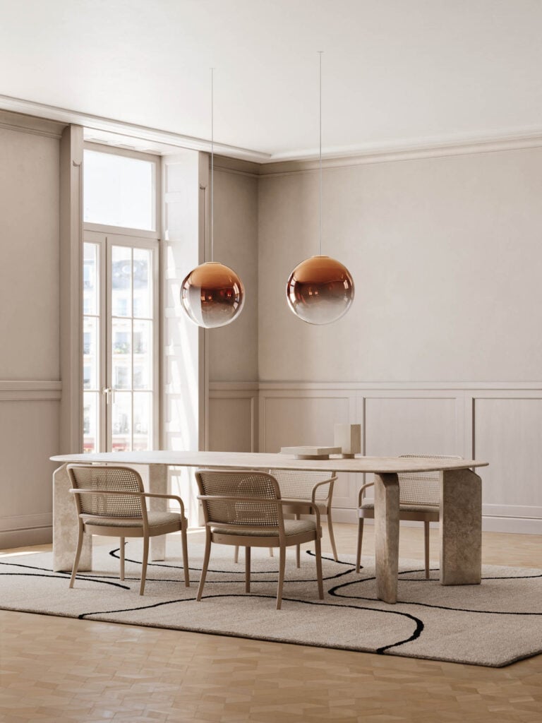 A minimalist dining room with a rectangular stone table, four rattan chairs, two spherical pendant lights, and large windows letting in natural light.