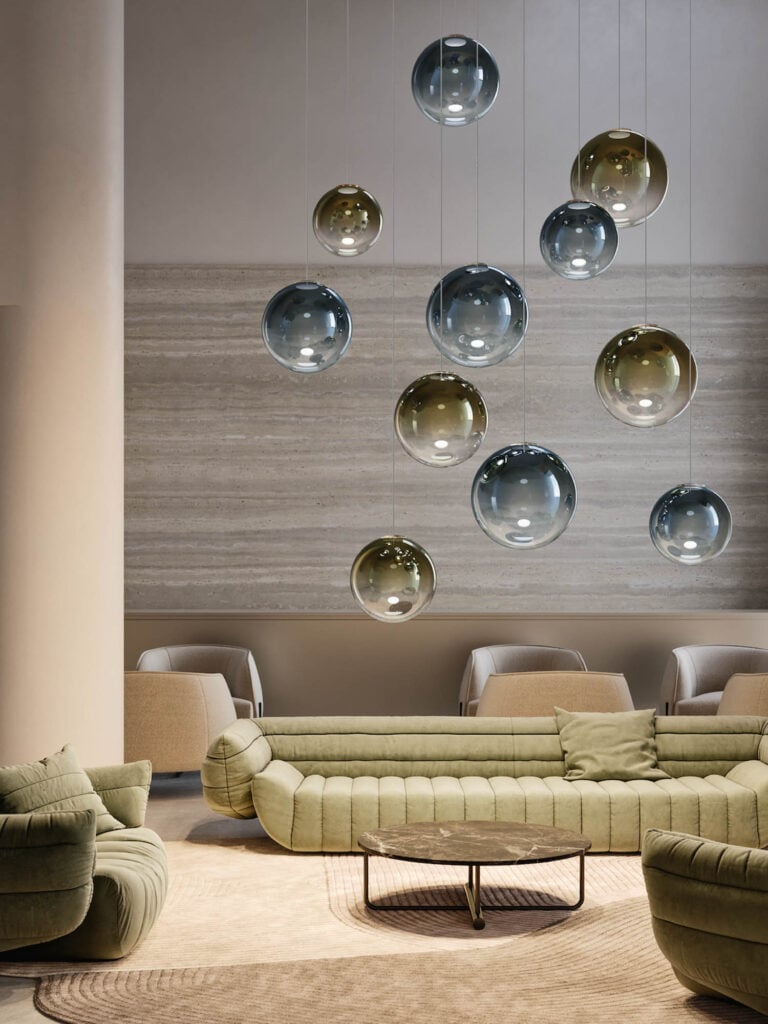 Modern lounge with olive green sofas, a round coffee table, and a cluster of glass pendant lights hanging from the ceiling. Neutral tones and minimalist design elements are featured.