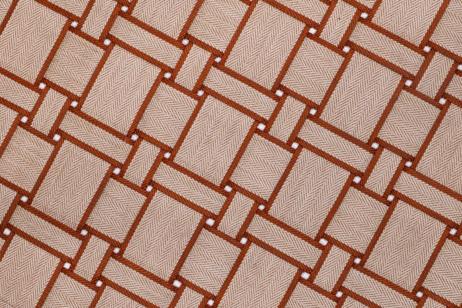 Close-up of a woven fabric with a geometric, interlocking pattern in shades of beige and brown, featuring small white dots at some intersections.