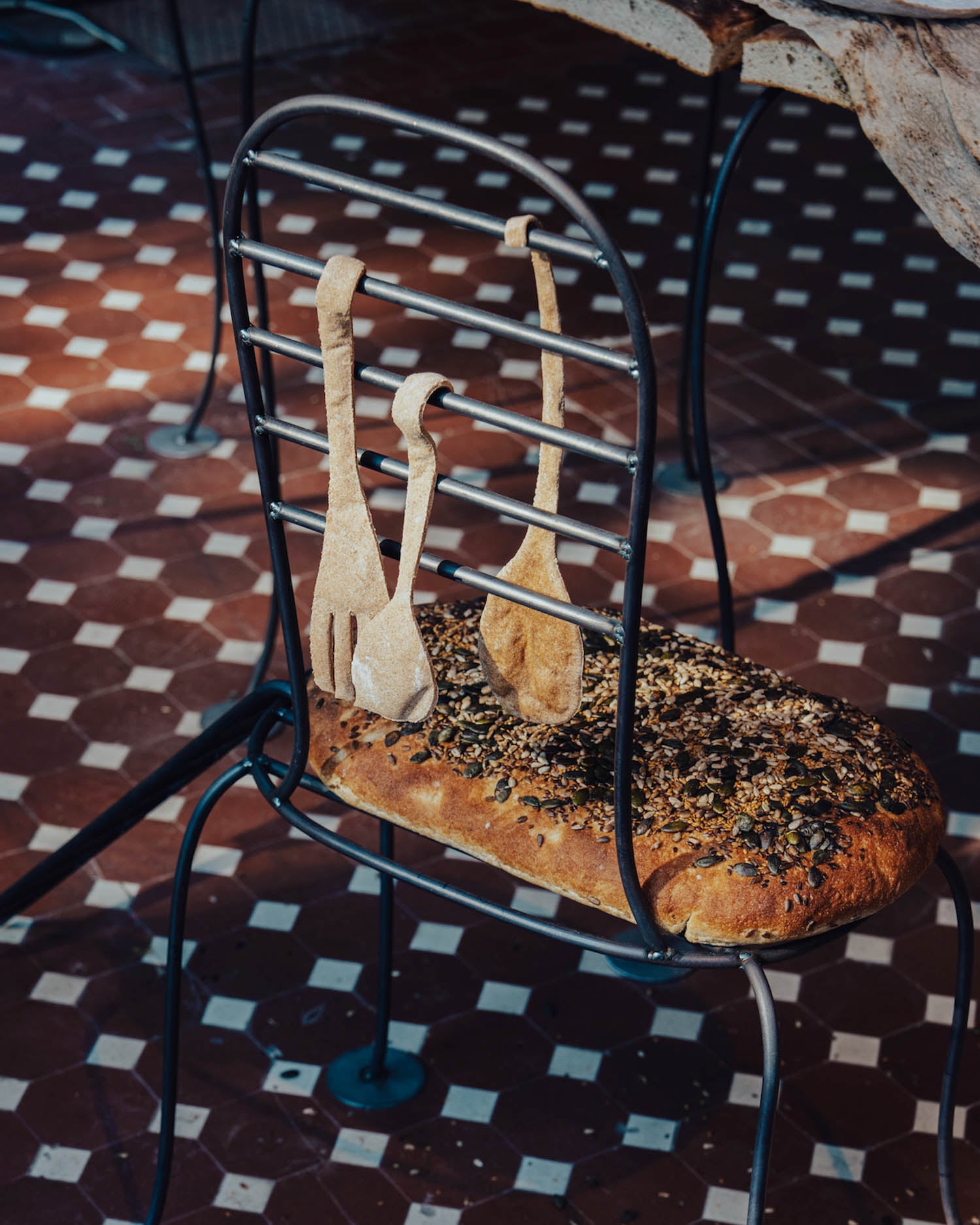 A metal chair with a seat made of seeded bread and bread shaped like a fork, knife, and spoon hanging on the backrest.