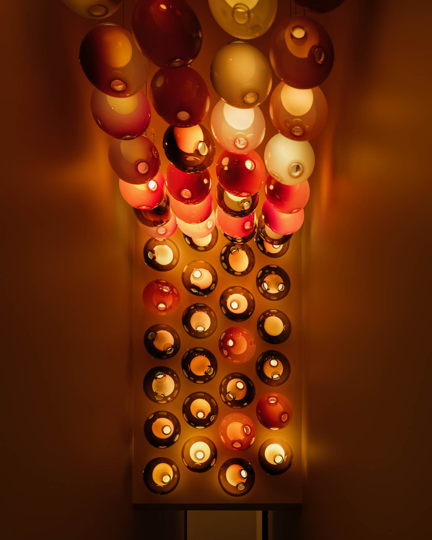 A ceiling installation featuring rows of round, red and white glass light fixtures, all illuminated and casting a warm ambient glow.