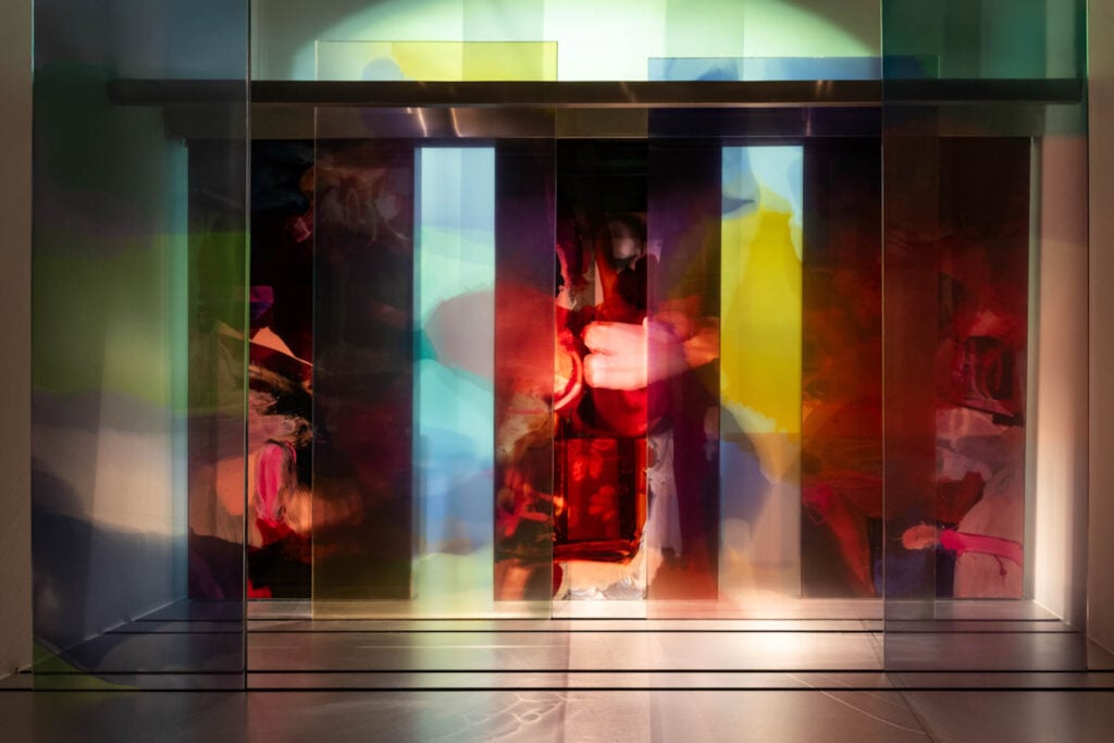 Colorful translucent panels stand upright in a row, casting overlapping red, yellow, blue, and green hues onto the background and floor.