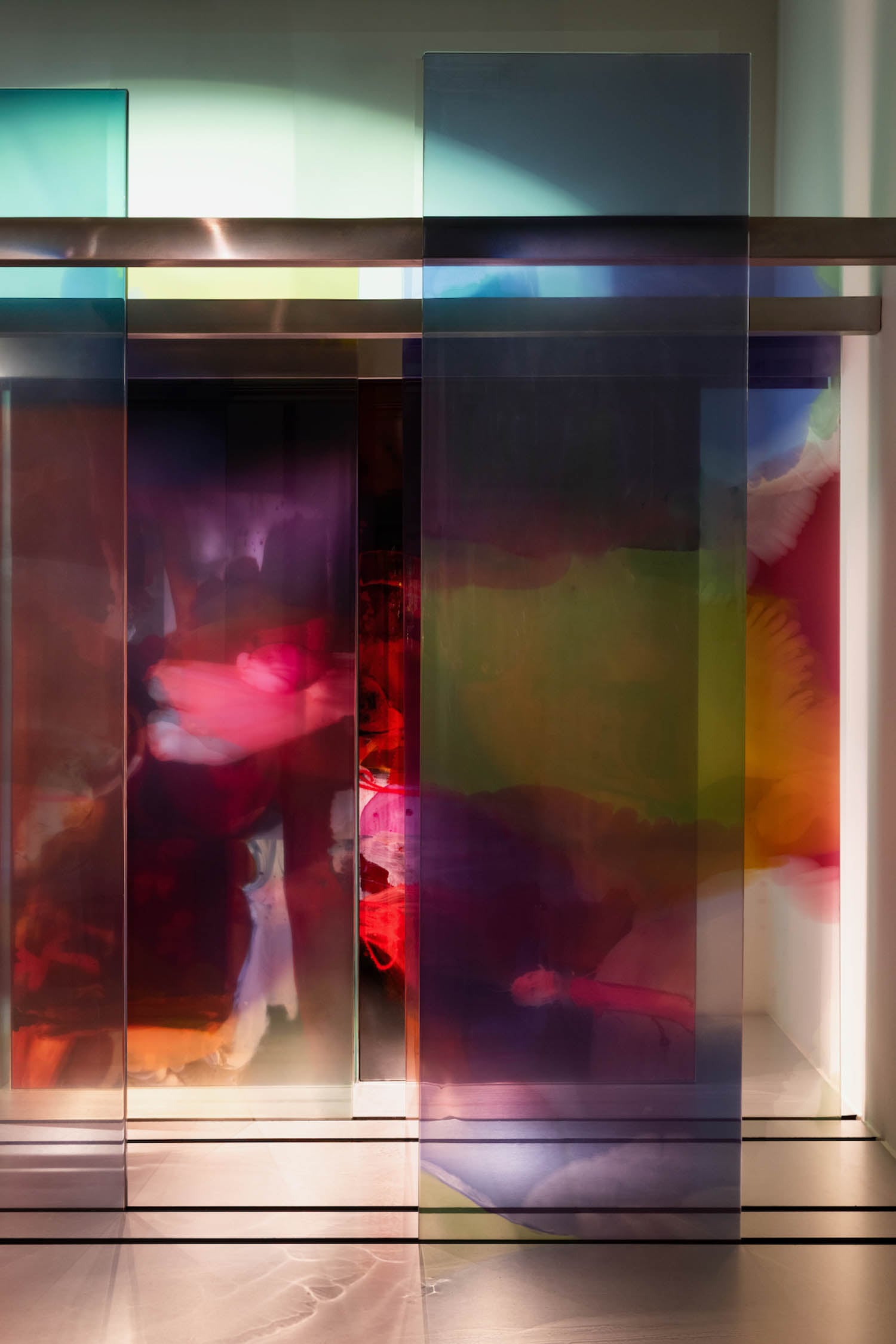 Colorful abstract art installation featuring tall, translucent panels with blurred, vibrant hues of red, purple, blue, and green, set against a softly lit background.