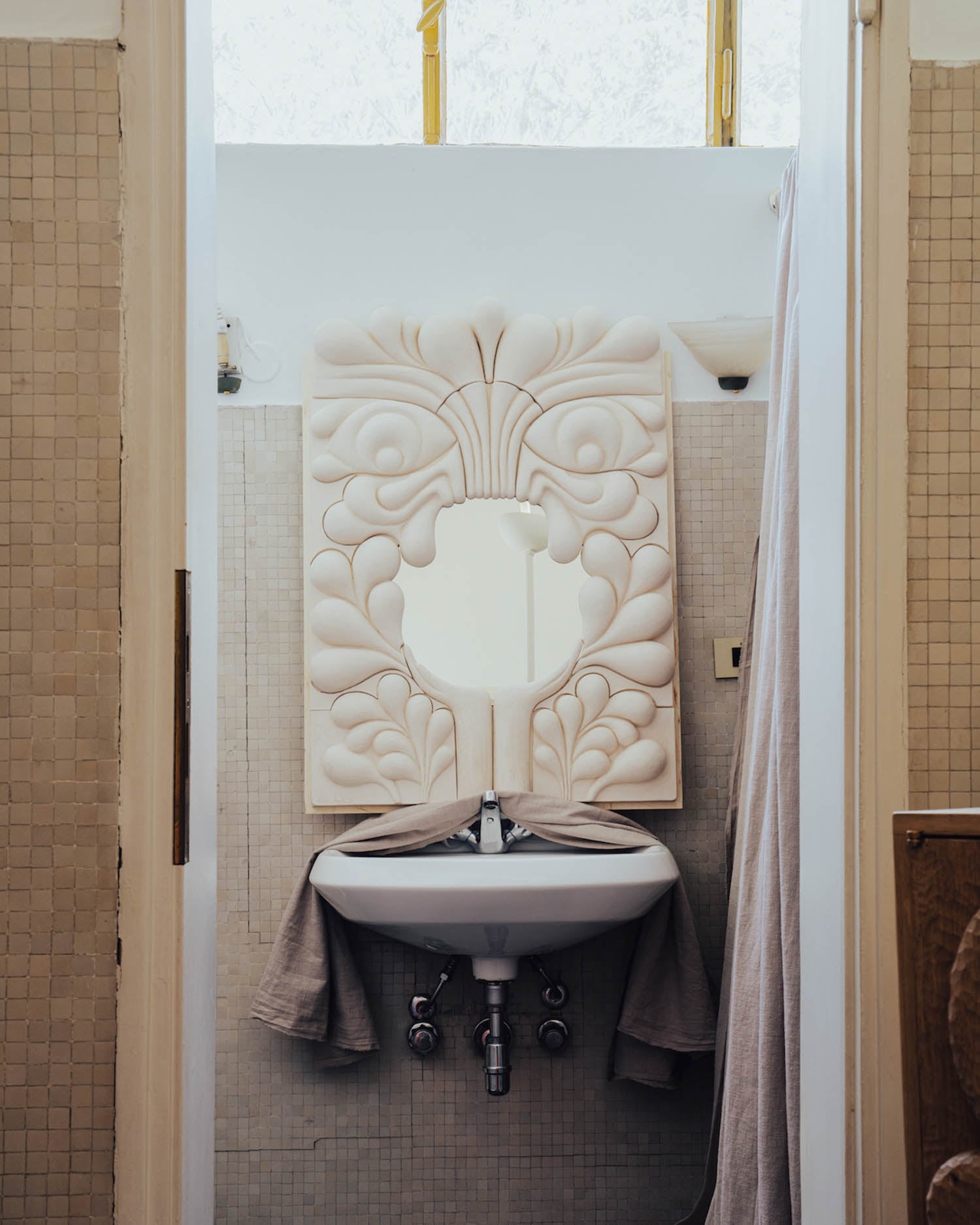 Small bathroom with a decorative mirror above a white sink, towels draped on both sides, and tiled walls in neutral tones.