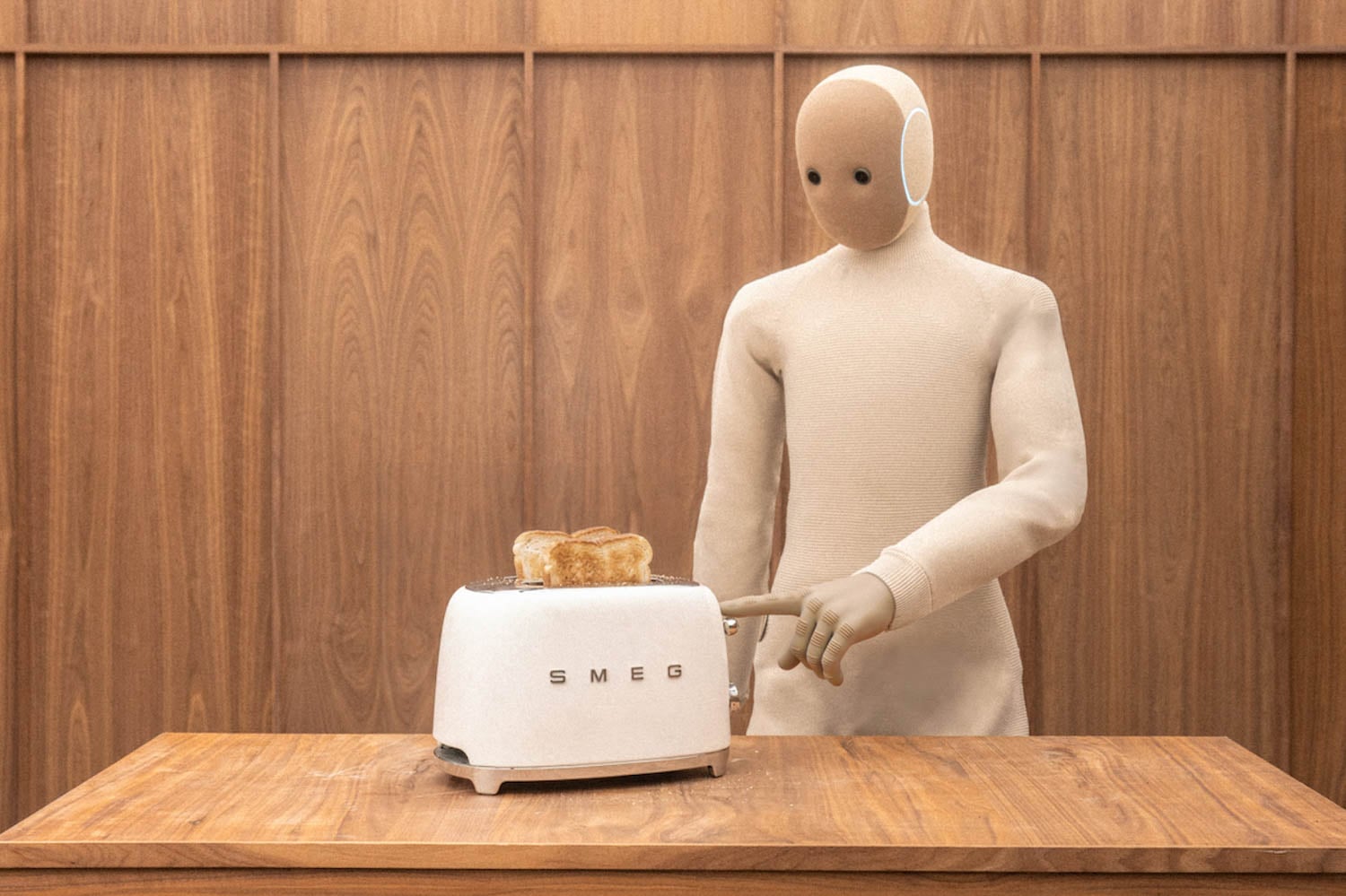 A humanoid figure in a beige suit presses the lever on a white SMEG toaster with two slices of toast, standing at a wooden counter in front of a wood-paneled wall.
