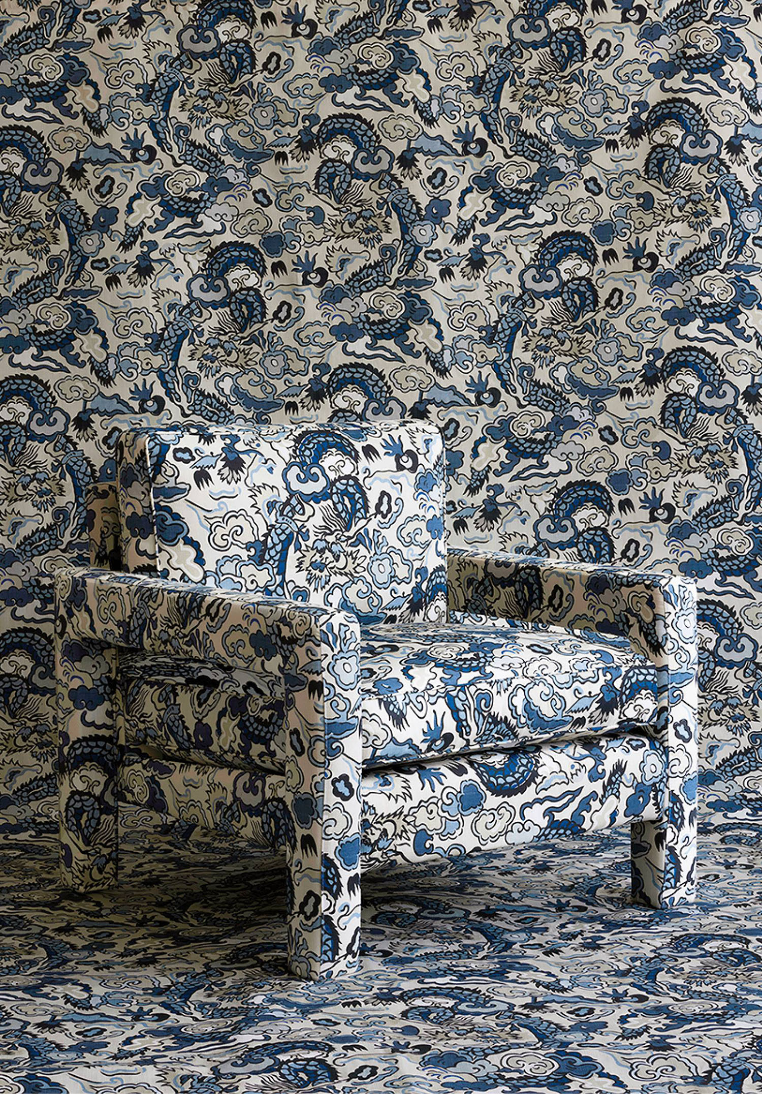 An armchair upholstered in blue and white patterned fabric sits against a wall covered in a matching pattern, making the chair blend into the background.