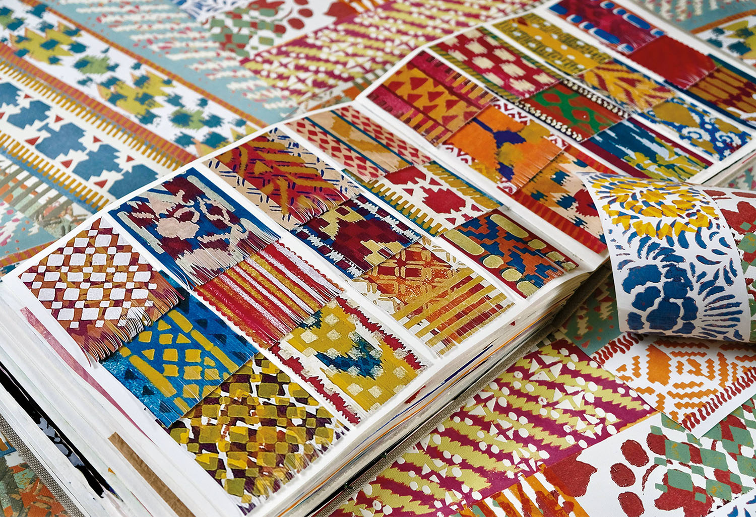 A sketchbook displays pages filled with colorful geometric and floral patterns, with additional patterned papers scattered around it.