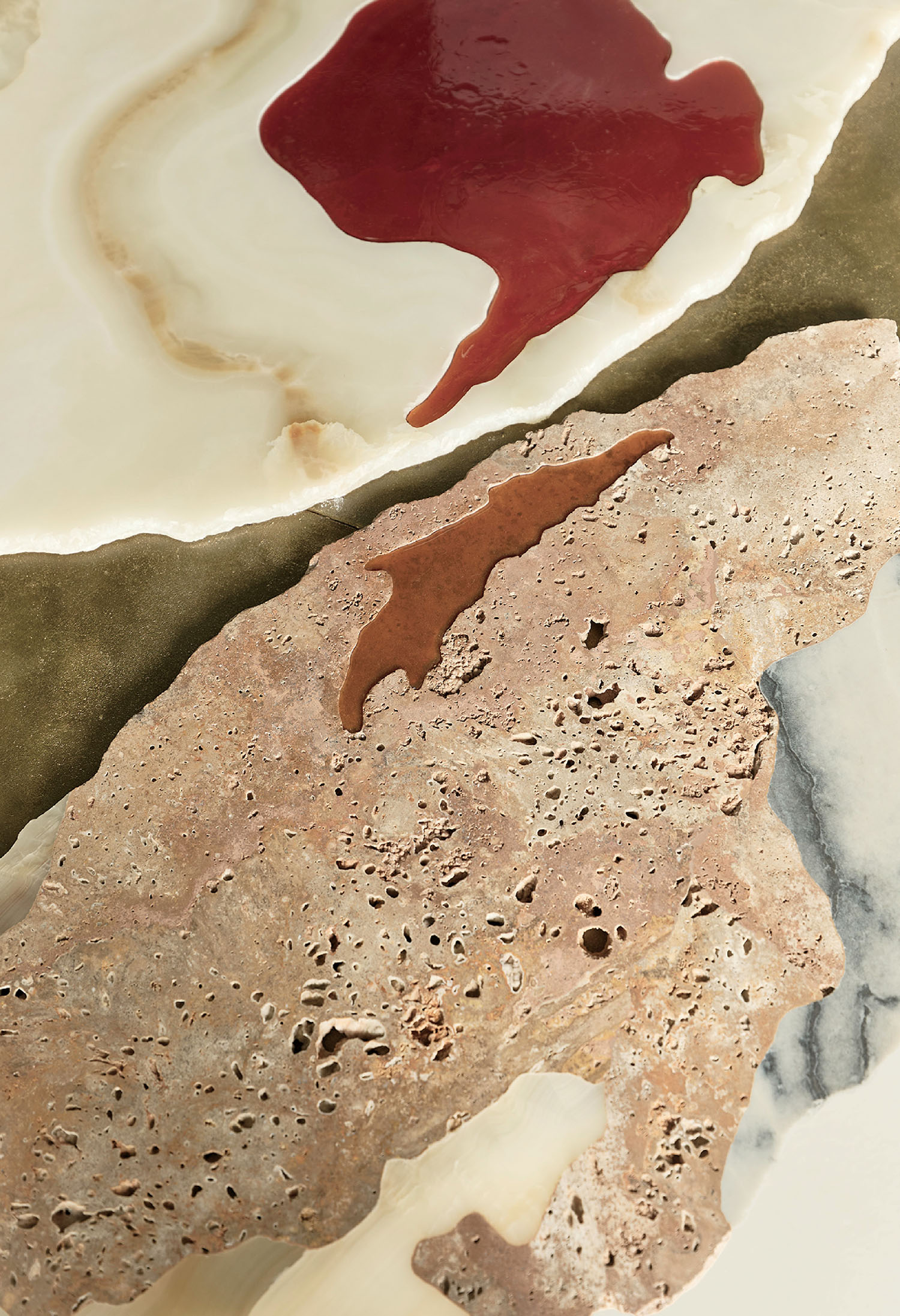 Close-up of textured stone surfaces in beige and cream tones, with smooth areas and red and brown irregular liquid stains on top.