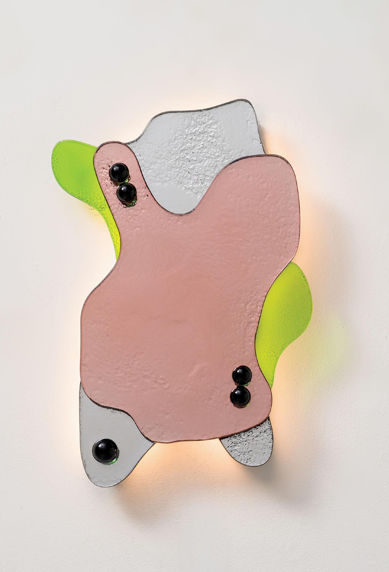 Abstract wall sculpture featuring overlapping shapes in pink, gray, and neon green with glossy black circular accents, mounted on a white wall.