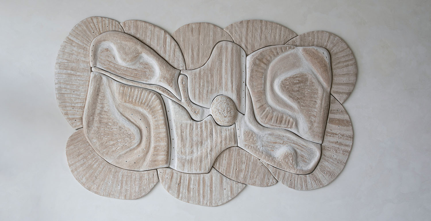 Textured wall sculpture composed of abstract, organic shapes in beige tones, assembled in an undulating, layered arrangement against a light background.