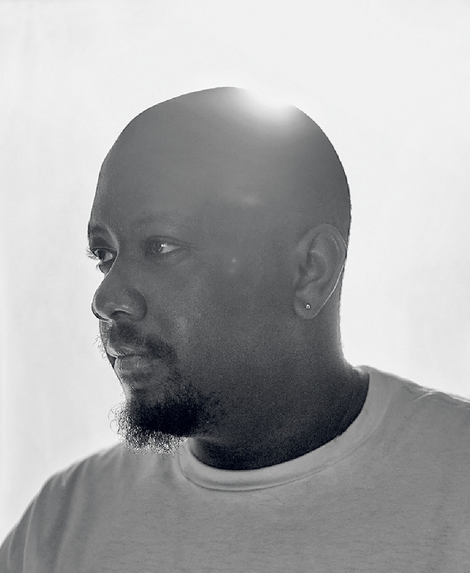 Black and white photo of a man in a white shirt with a short beard, looking to the left, with sunlight visible behind his head.