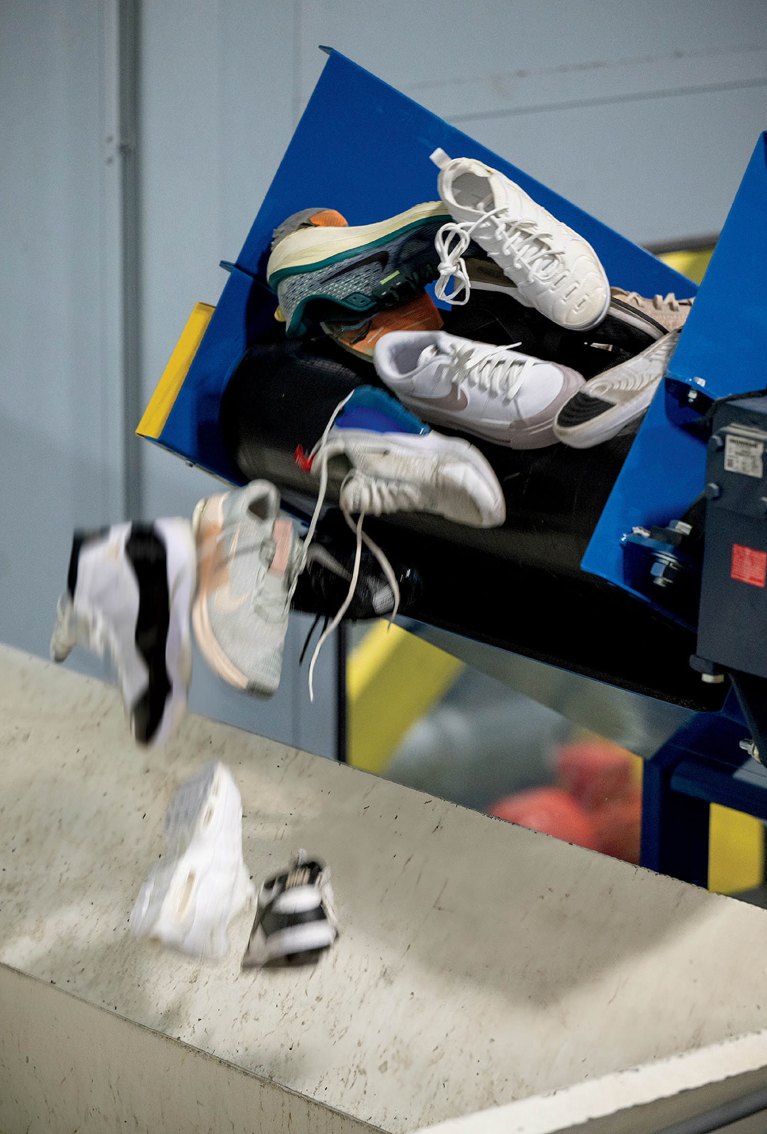 A conveyor belt releases several pairs of sneakers, dropping them onto a surface below inside an industrial facility.