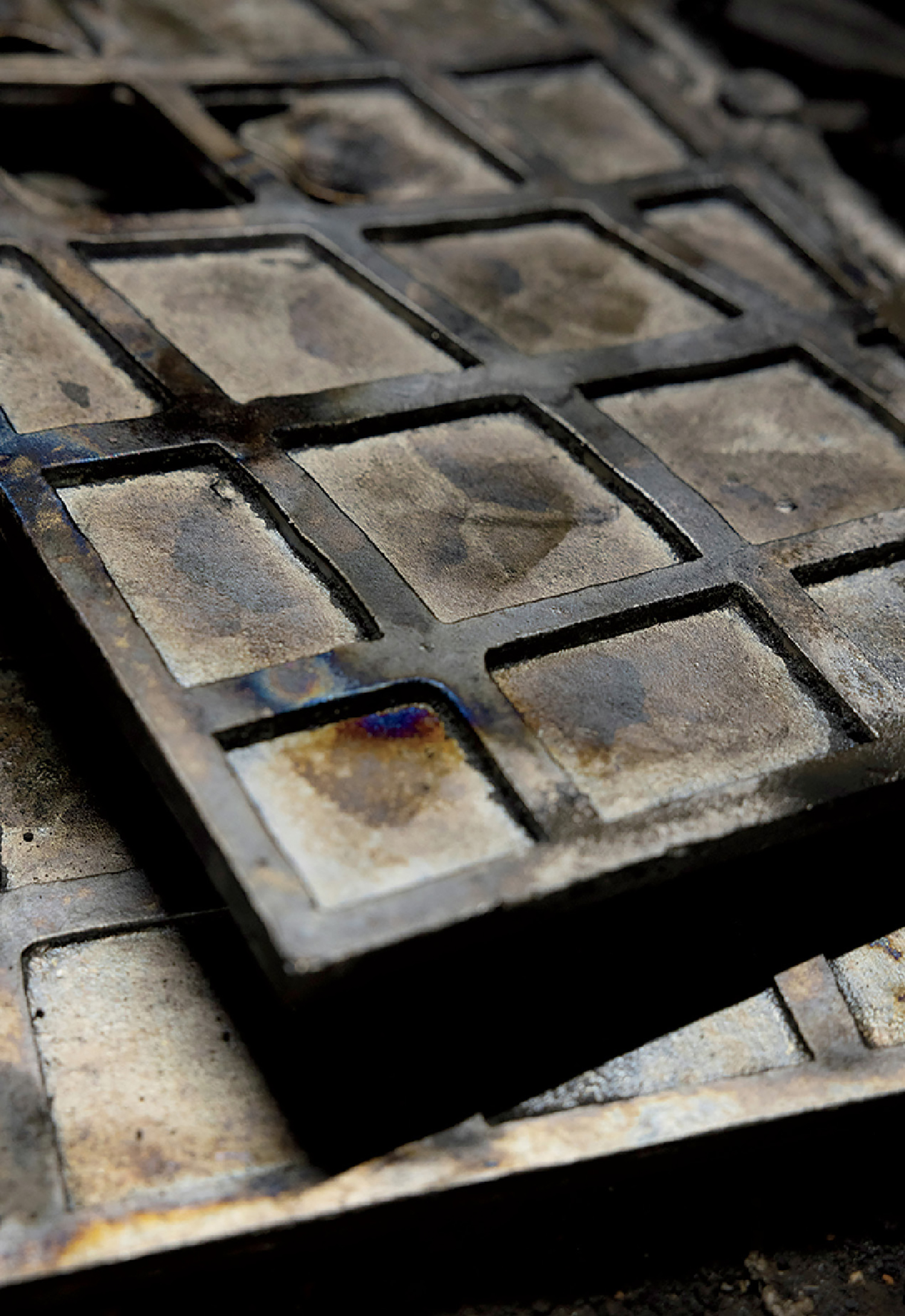 Close-up of two weathered, rectangular metal plates with square grid patterns, stacked on top of each other, showing signs of rust and discoloration.