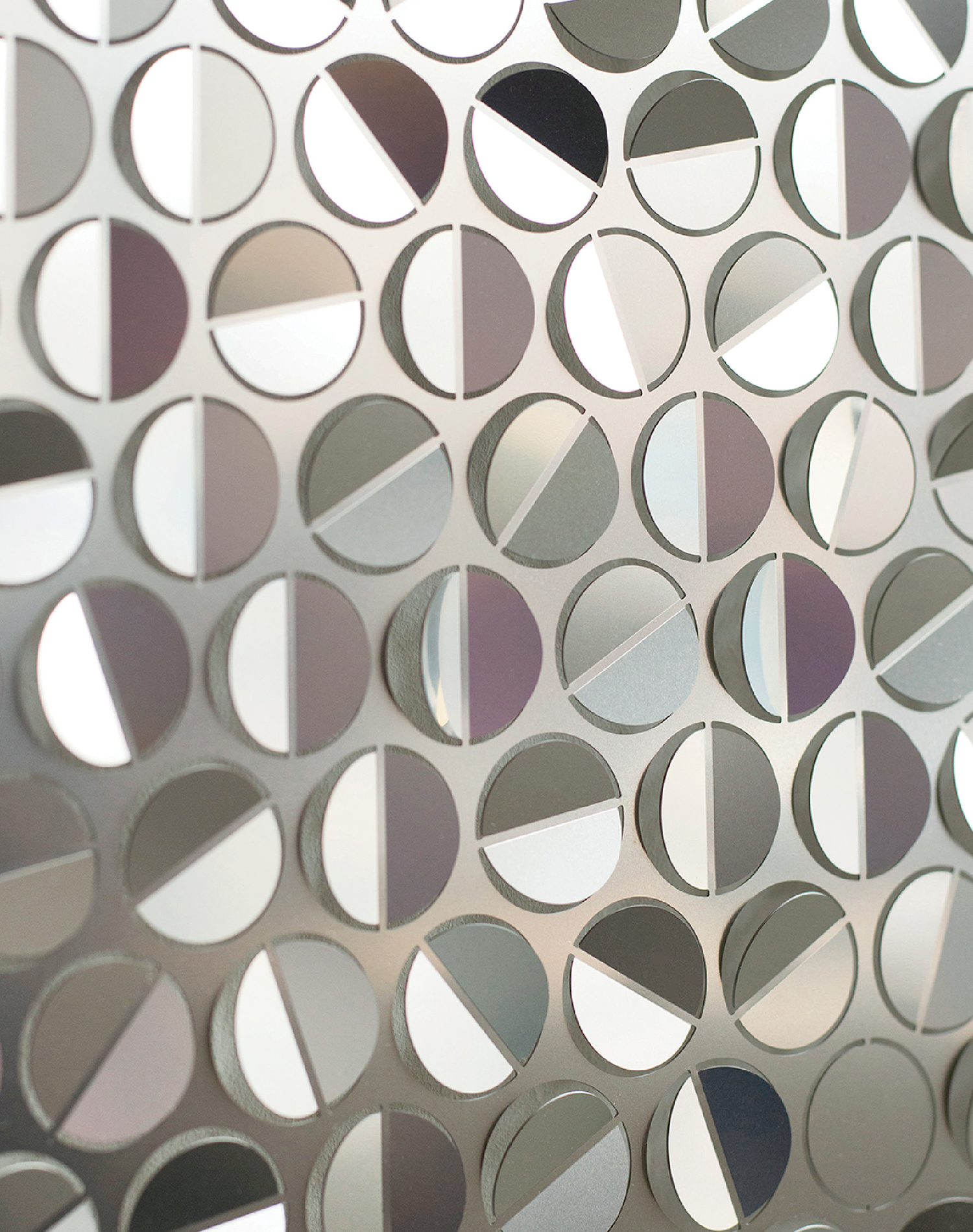 A close-up of a metallic surface with a repeating pattern of circular cutouts, each partly covered by a rotating half-disc, creating geometric reflections.