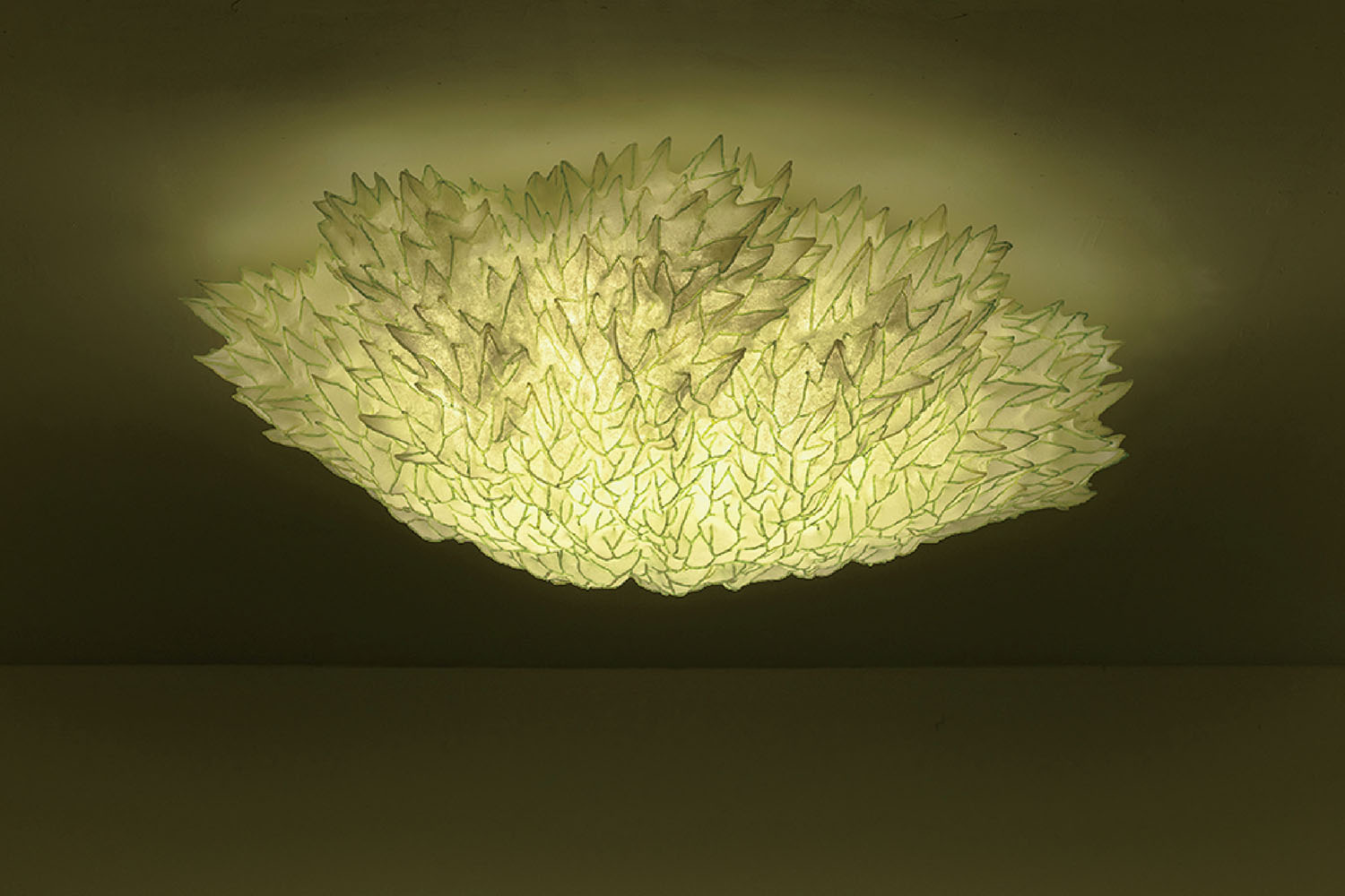 A ceiling light fixture with a clustered design of overlapping, translucent, leaf-like shapes emitting a soft, warm glow.