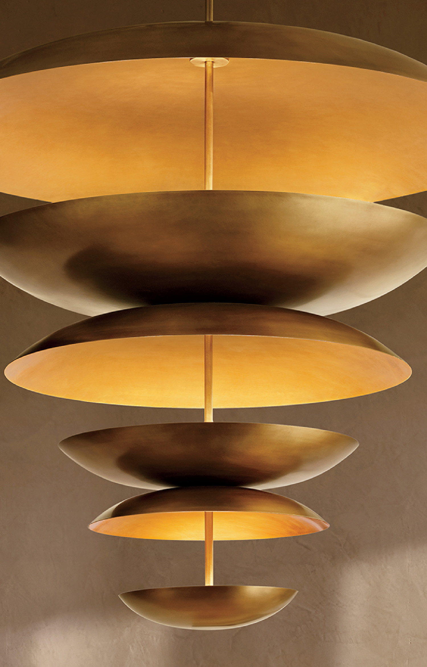 A modern chandelier with multiple large, circular, gold-toned discs arranged in a descending pattern, emitting a warm yellow light.