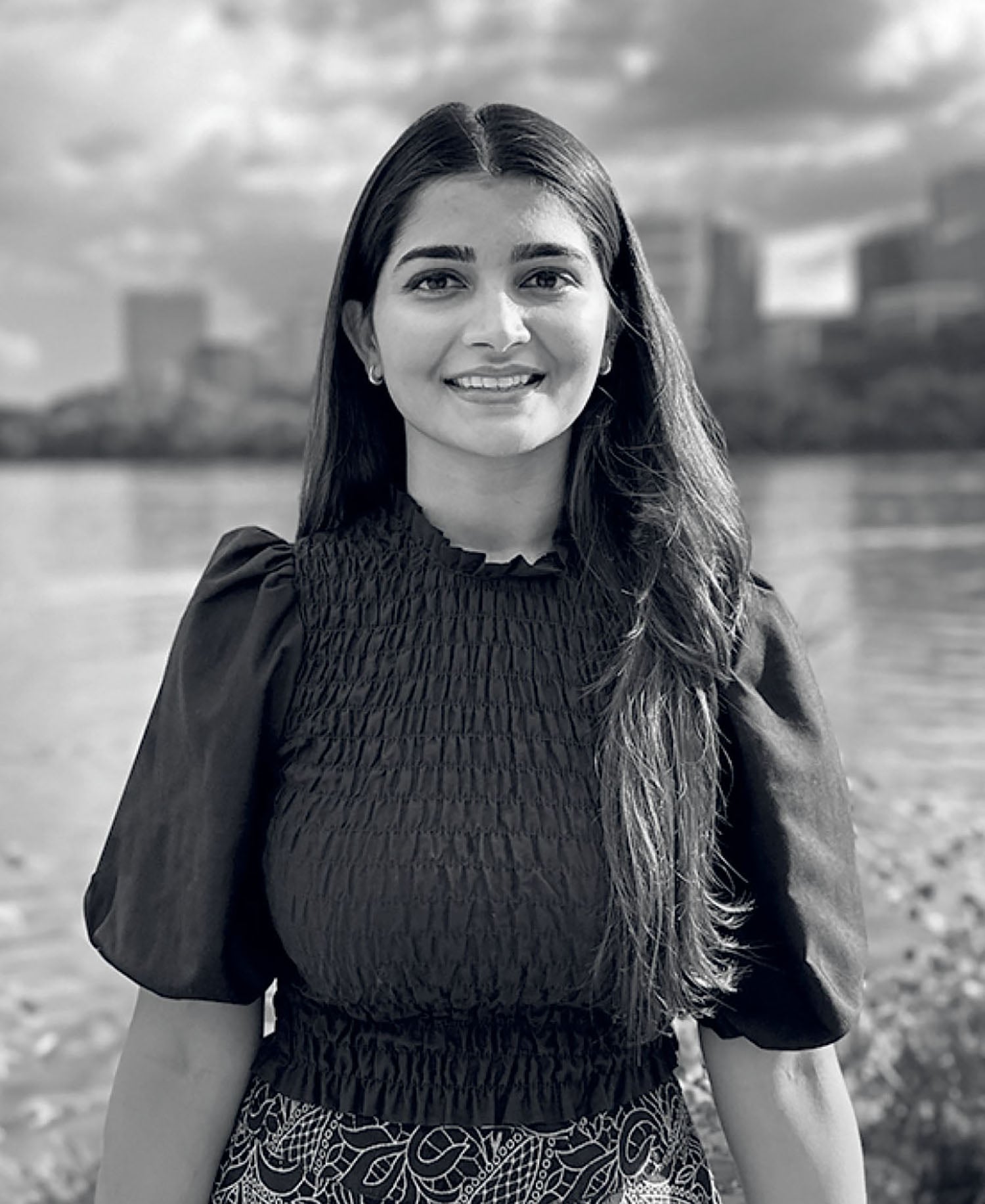 A woman standing by the water with a city in the background.
