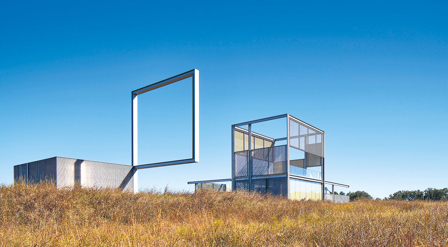 Modern architectural structures with geometric forms stand in a grassy field under a clear blue sky.