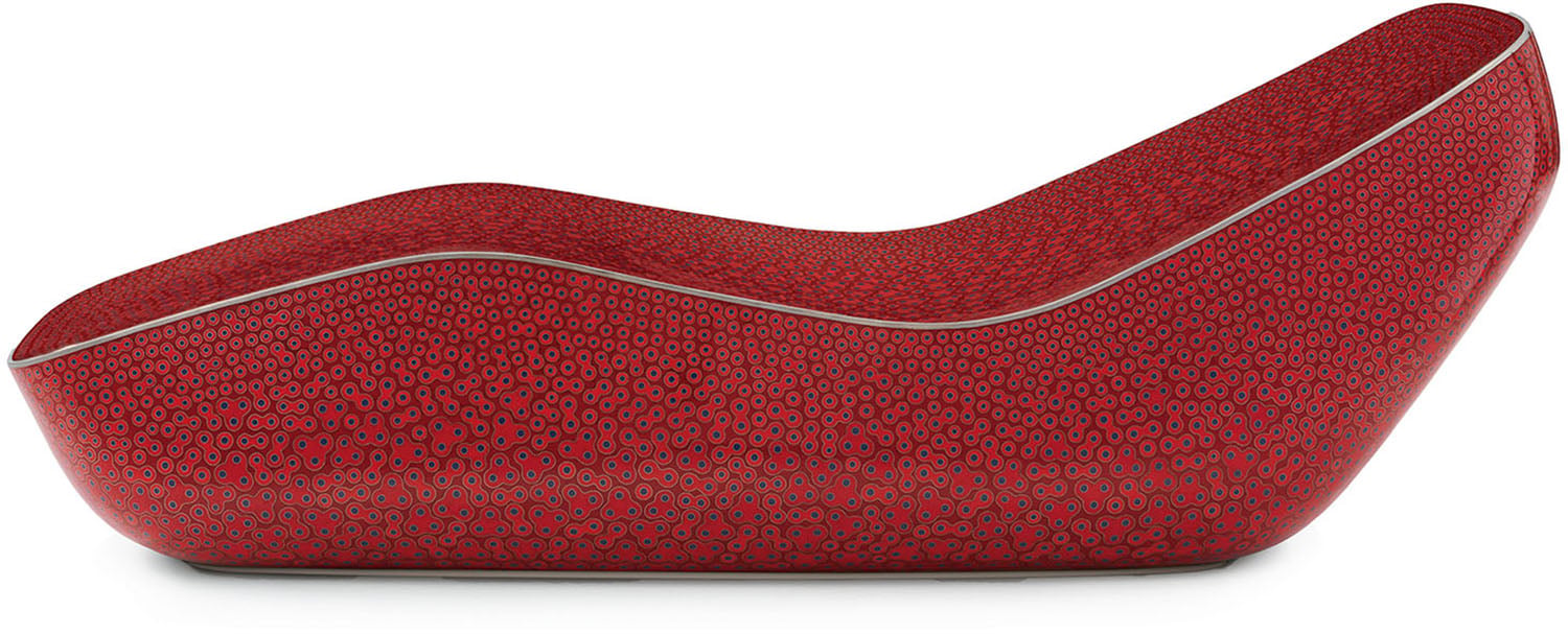 A modern, red chaise lounge with a curvy, ergonomic design and a textured pattern of small circular shapes.