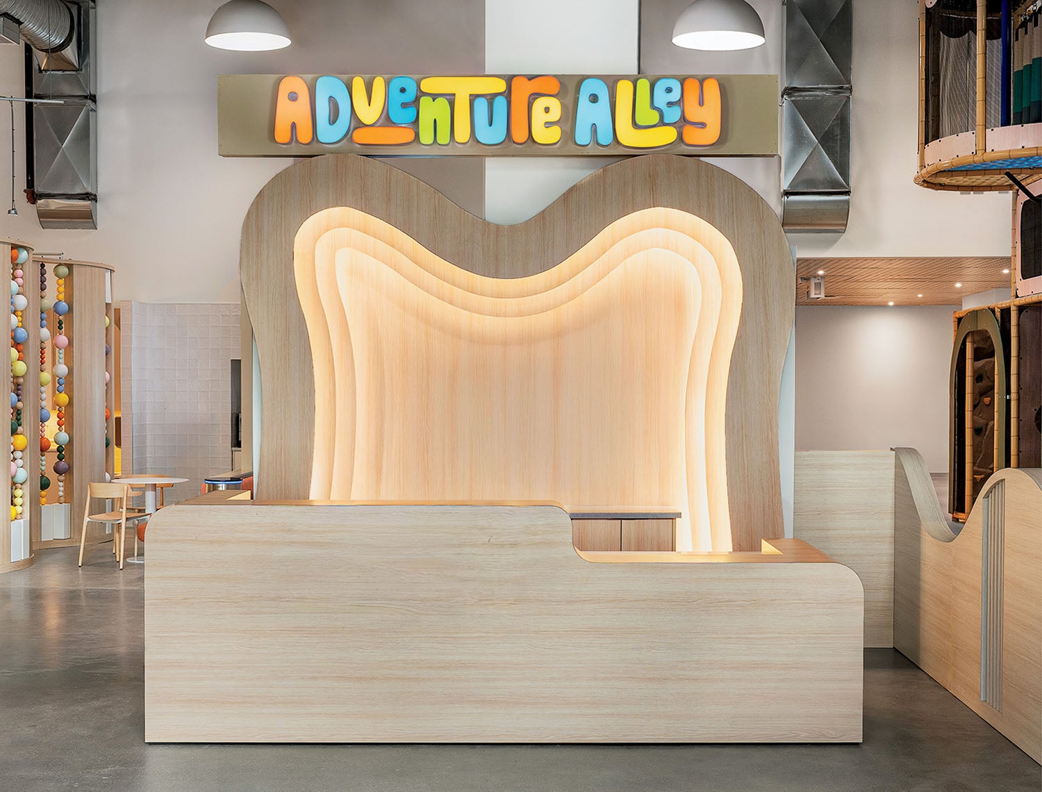 Reception desk with layered wood design beneath a colorful "Adventure Alley" sign in a modern, playful indoor space.