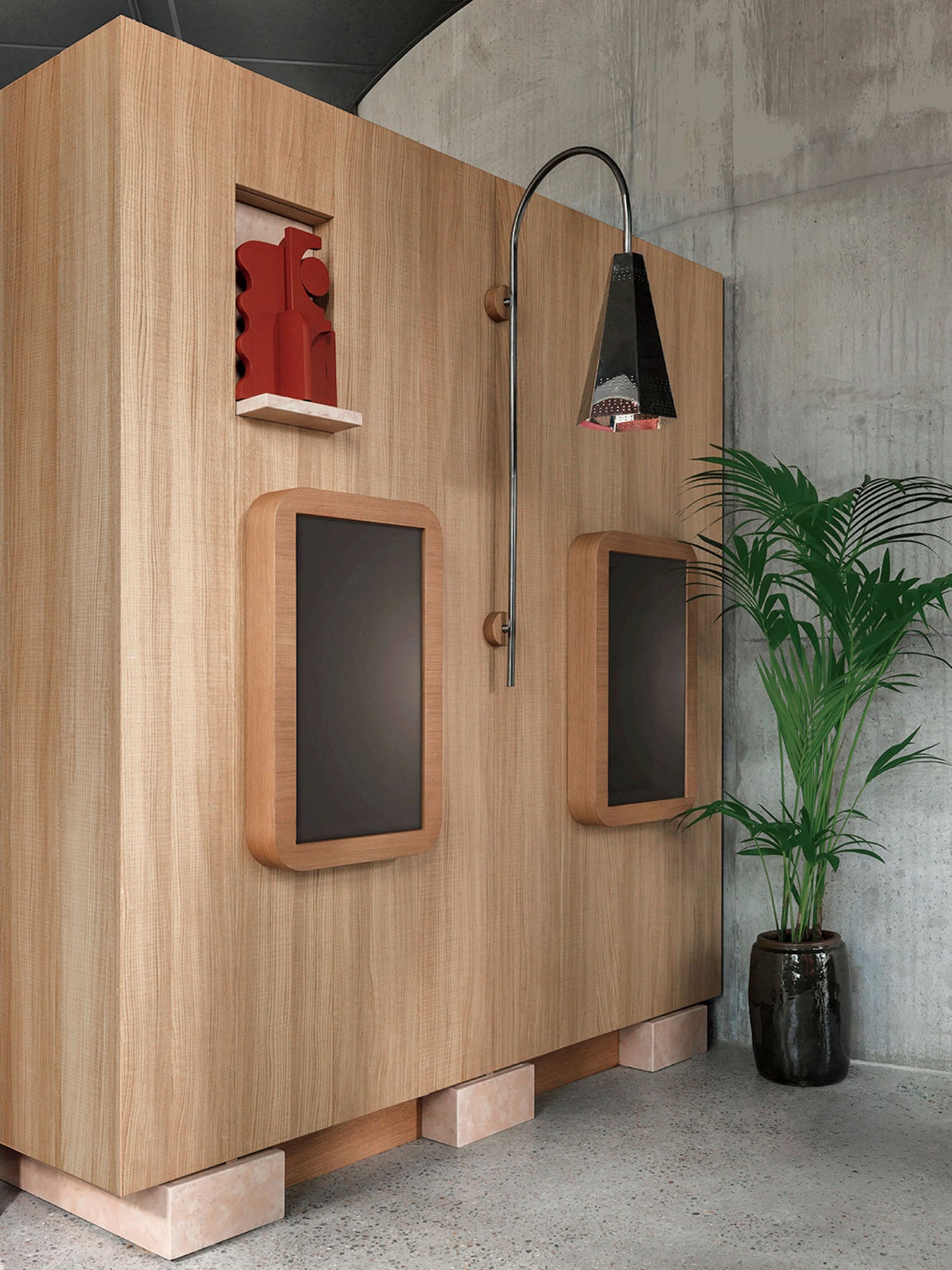 A modern wooden structure with two large black screens, a built-in red decorative piece, an overhead lamp, and a potted green plant beside it against a concrete wall.