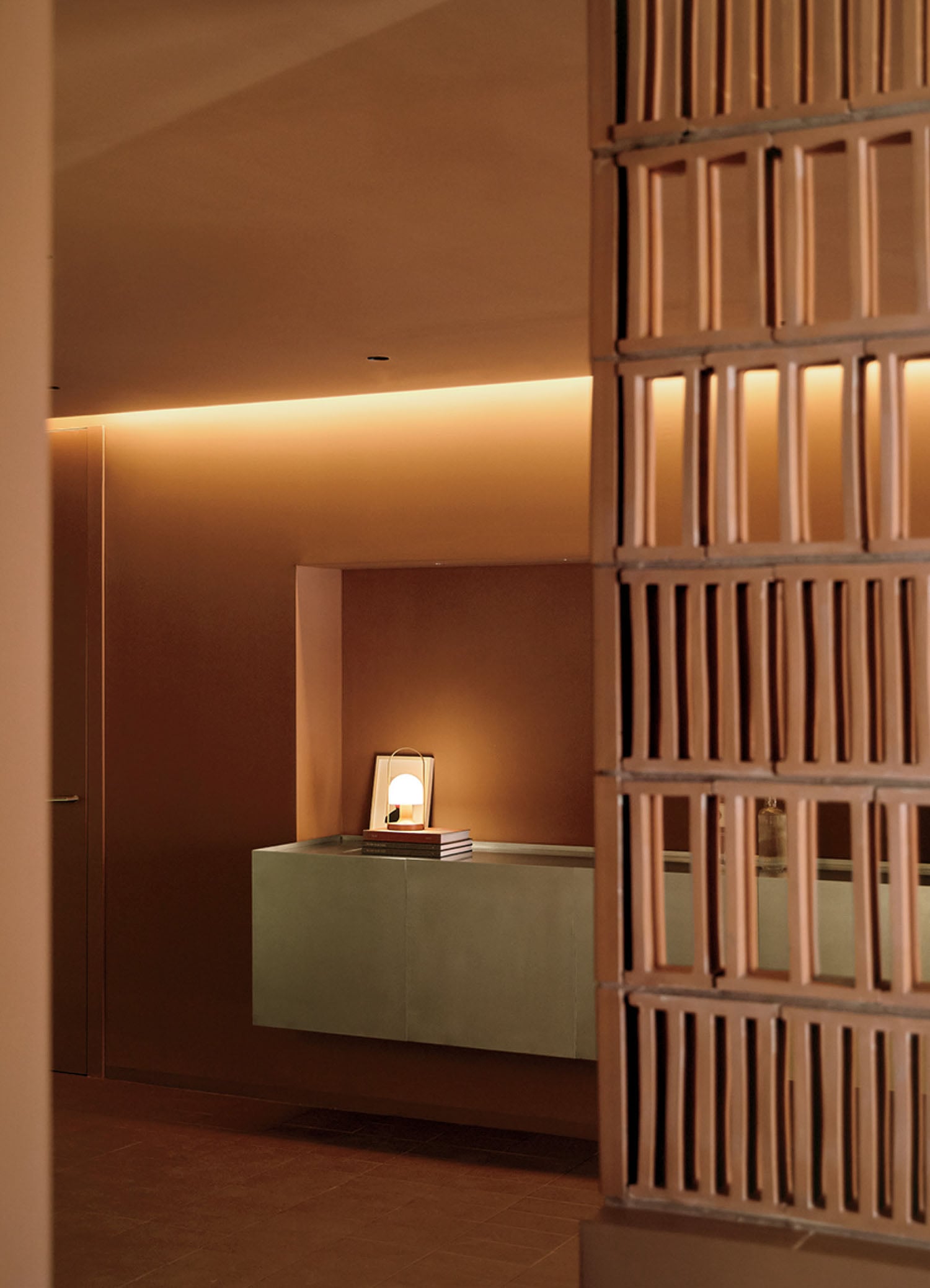 Minimalist interior with warm lighting, a floating shelf holding stacked books and a modern lamp, and a decorative partition in the foreground.