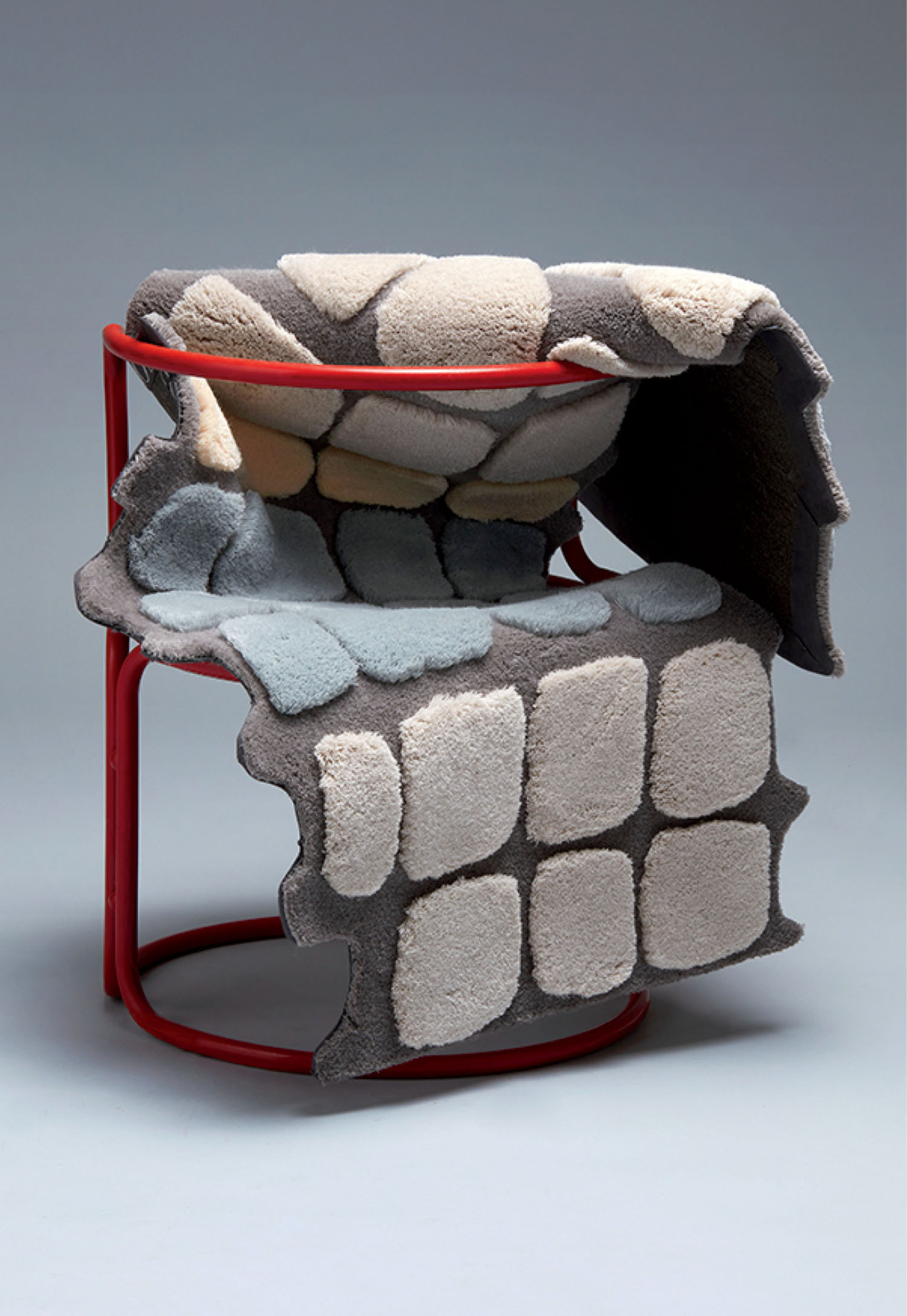 A red metal chair is draped with a thick, textured covering resembling irregular stone or cobblestone patterns in gray, beige, and light blue tones.