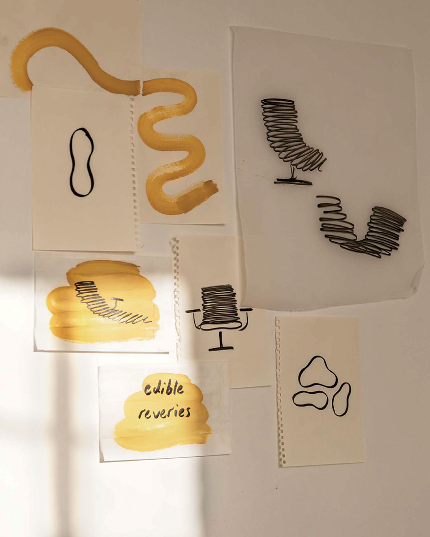 Several abstract line and paint drawings on white paper are taped to a wall, featuring yellow brushstrokes, black squiggles, and the handwritten words "edible reveries.