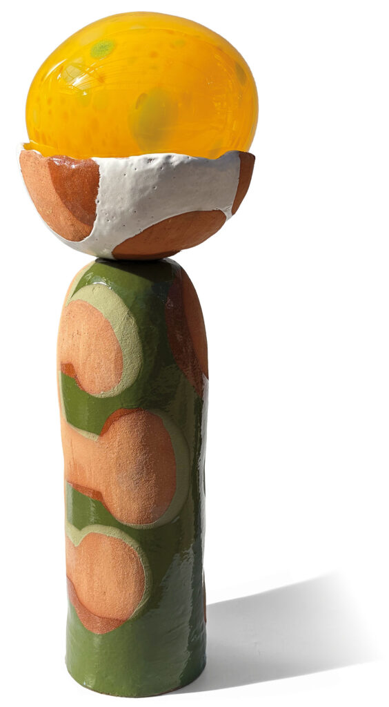 A colorful ceramic sculpture with a glossy yellow oval top, a white and brown speckled middle, and a tall green and brown base, standing on a white background.