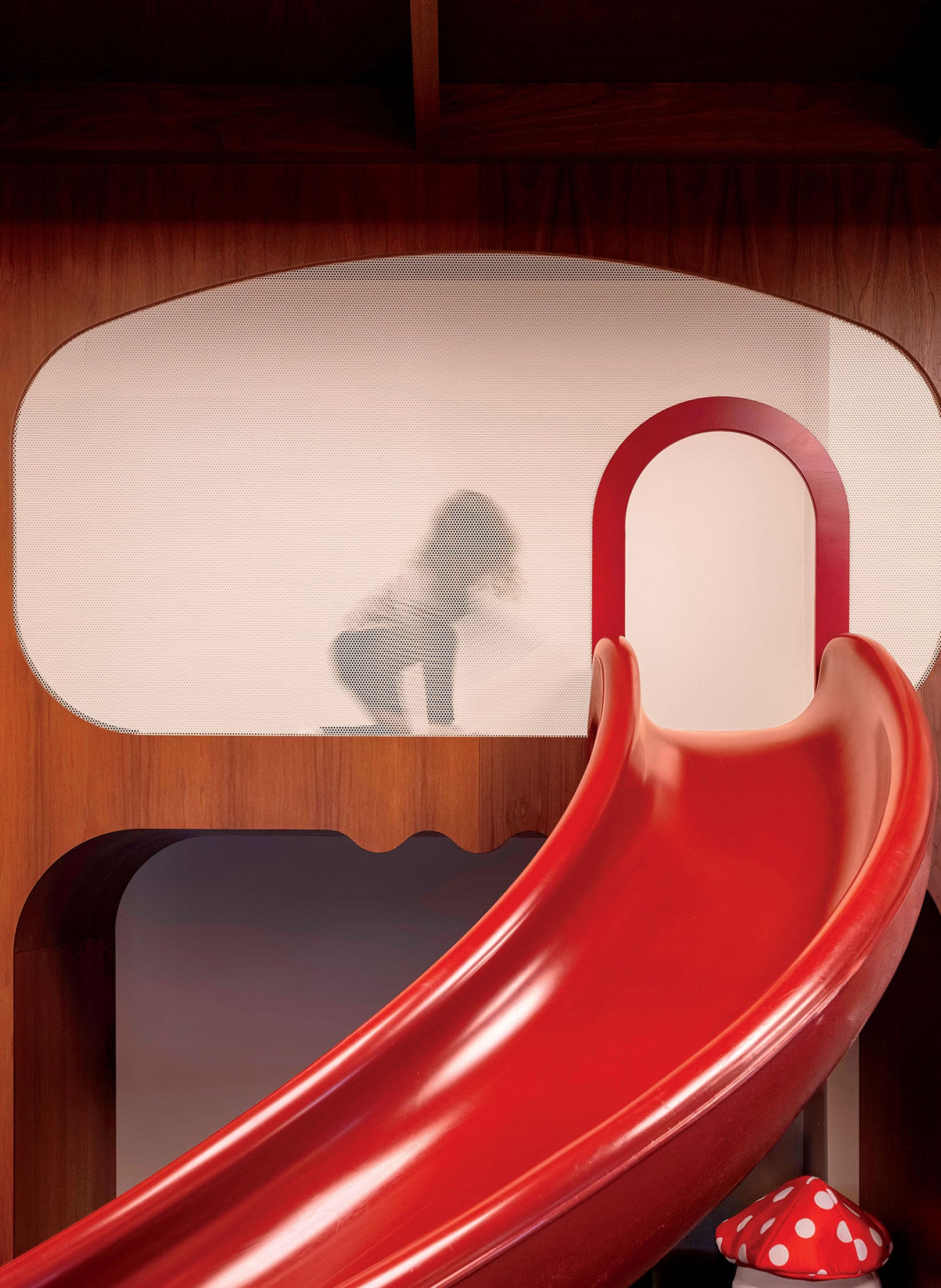 A red slide in a room with a white wall.