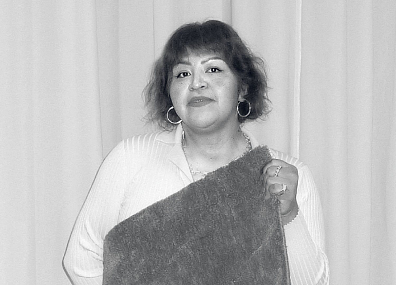 A person with short hair and hoop earrings stands in front of curtains, holding a textured rectangular object.