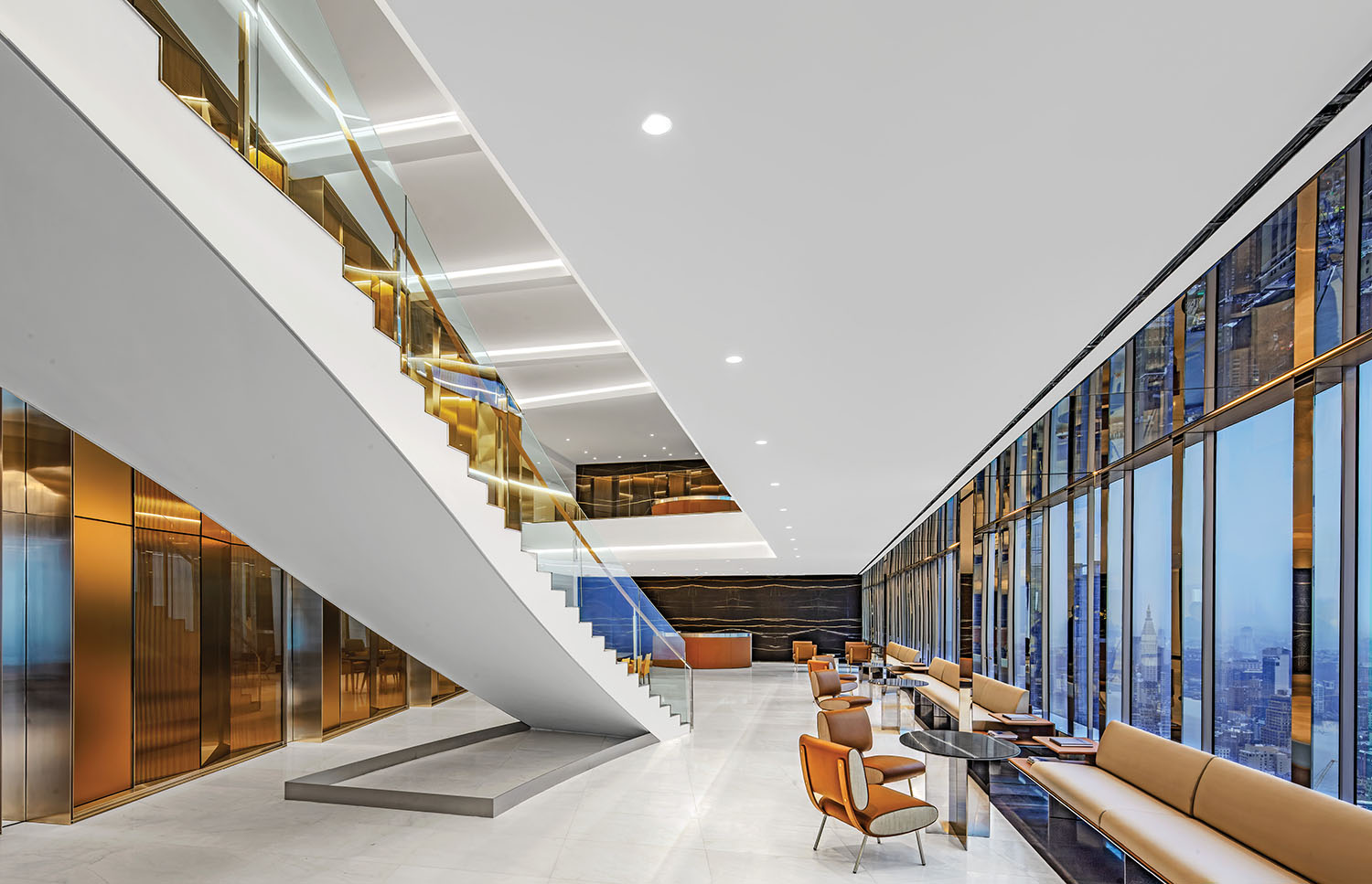 Modern office lobby with a white staircase, gold accents, floor-to-ceiling windows, beige seating, and cityscape views through the glass walls.