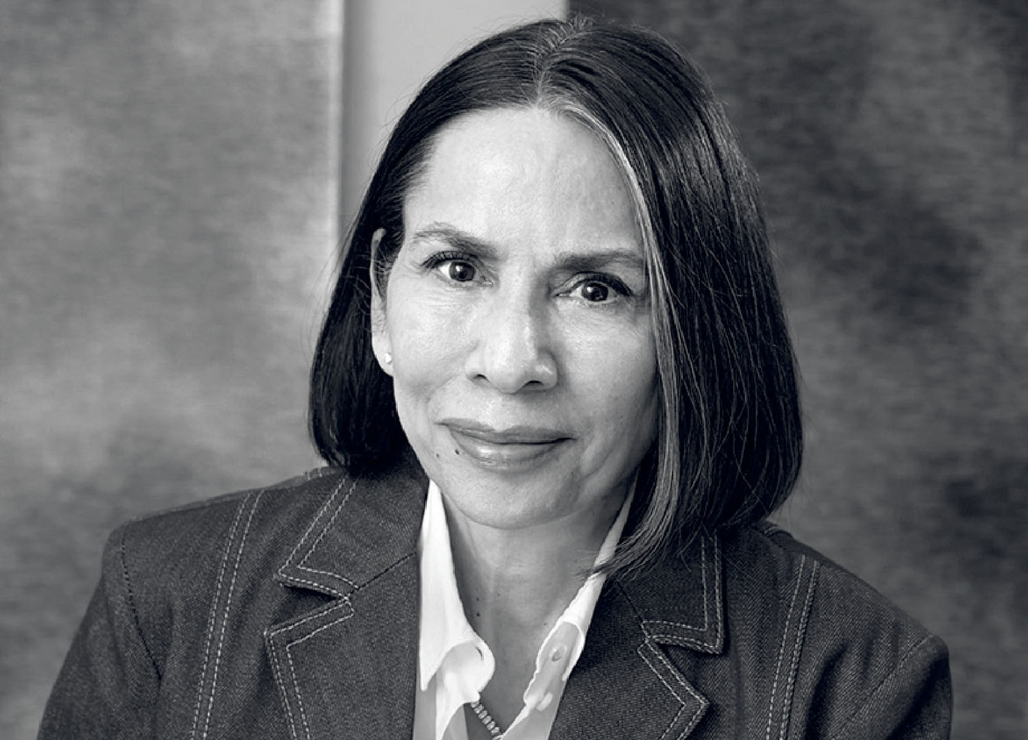 A woman with straight dark hair, wearing a blazer and a white shirt, looks at the camera with a neutral expression in a black and white portrait.