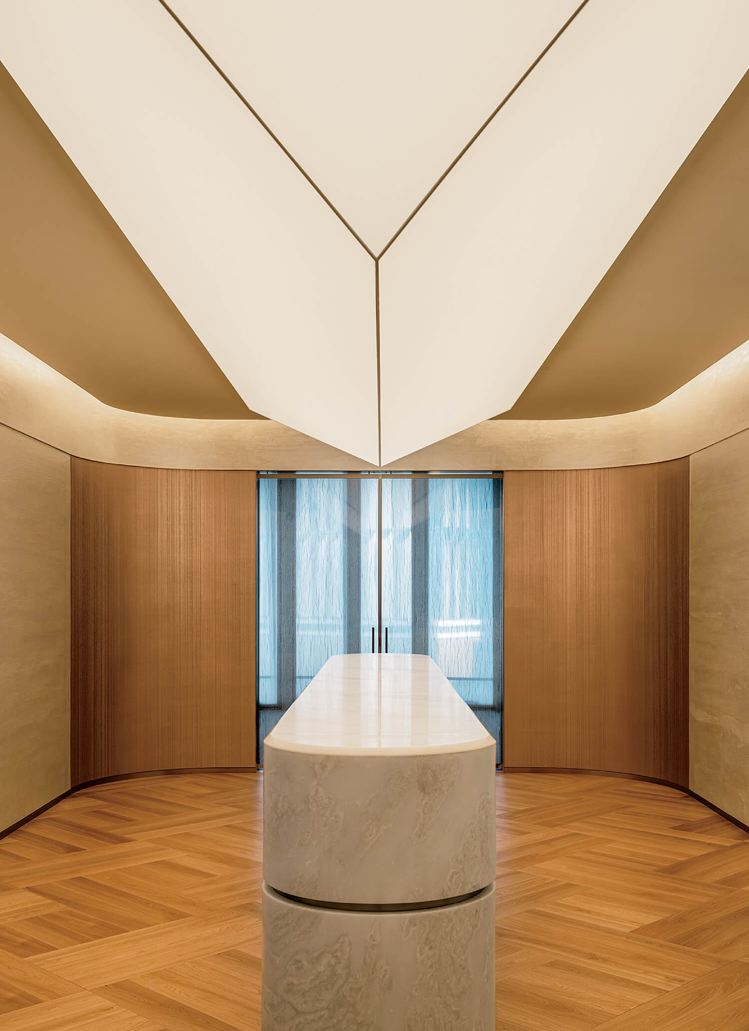 A modern interior with a white marble reception desk, wooden walls and floor, and a geometric ceiling with recessed lighting. Blue-tinted glass doors are in the background.